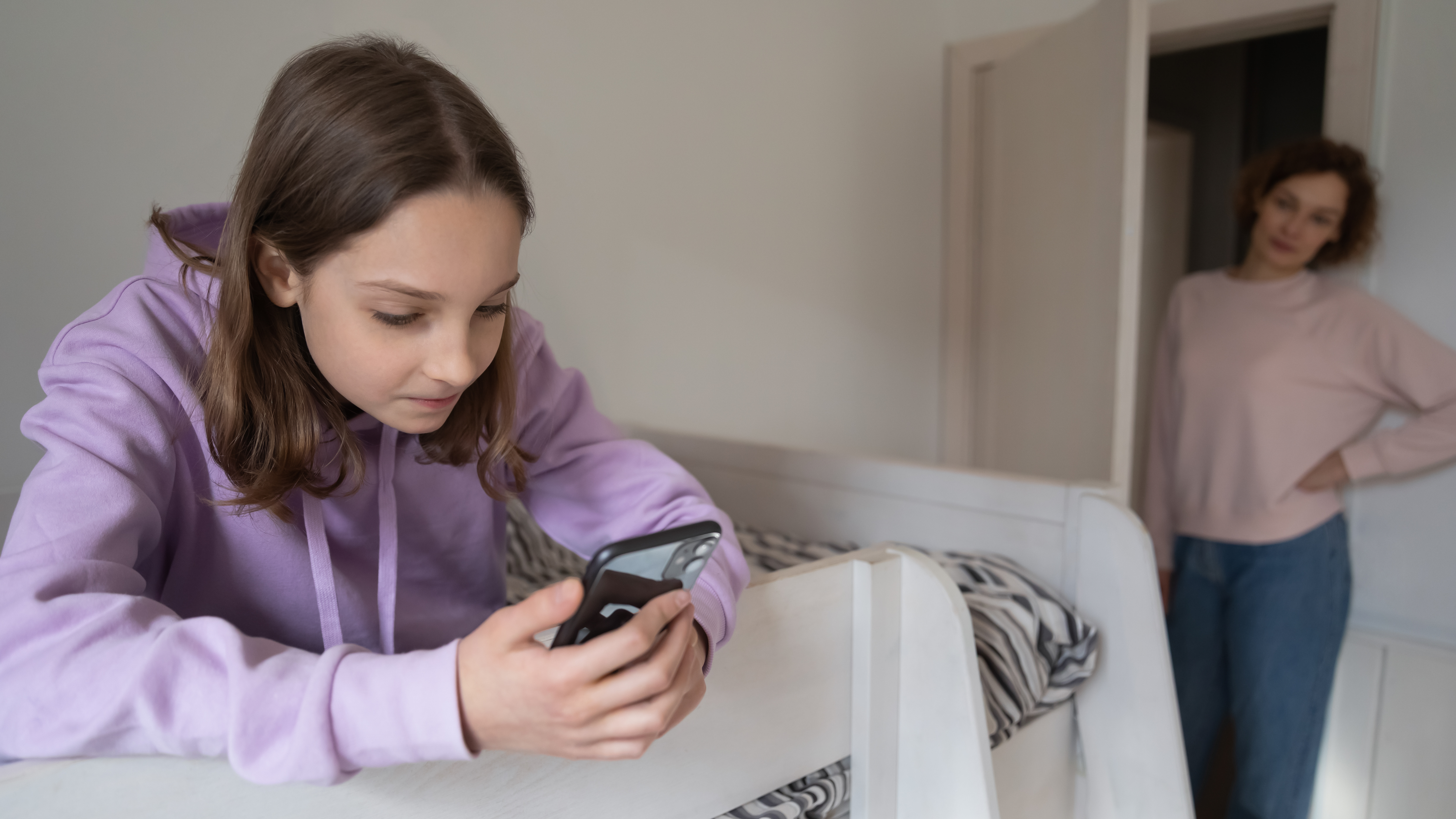 Uma garota usando um telefone enquanto uma mulher a observa |  Fonte: Shutterstock