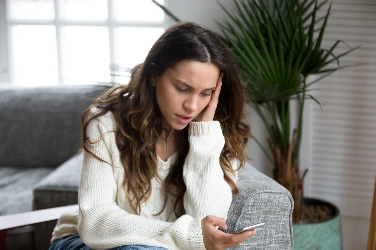 Une femme se sentant contrariée en lisant des messages sur un smartphone | Source : Shutterstock