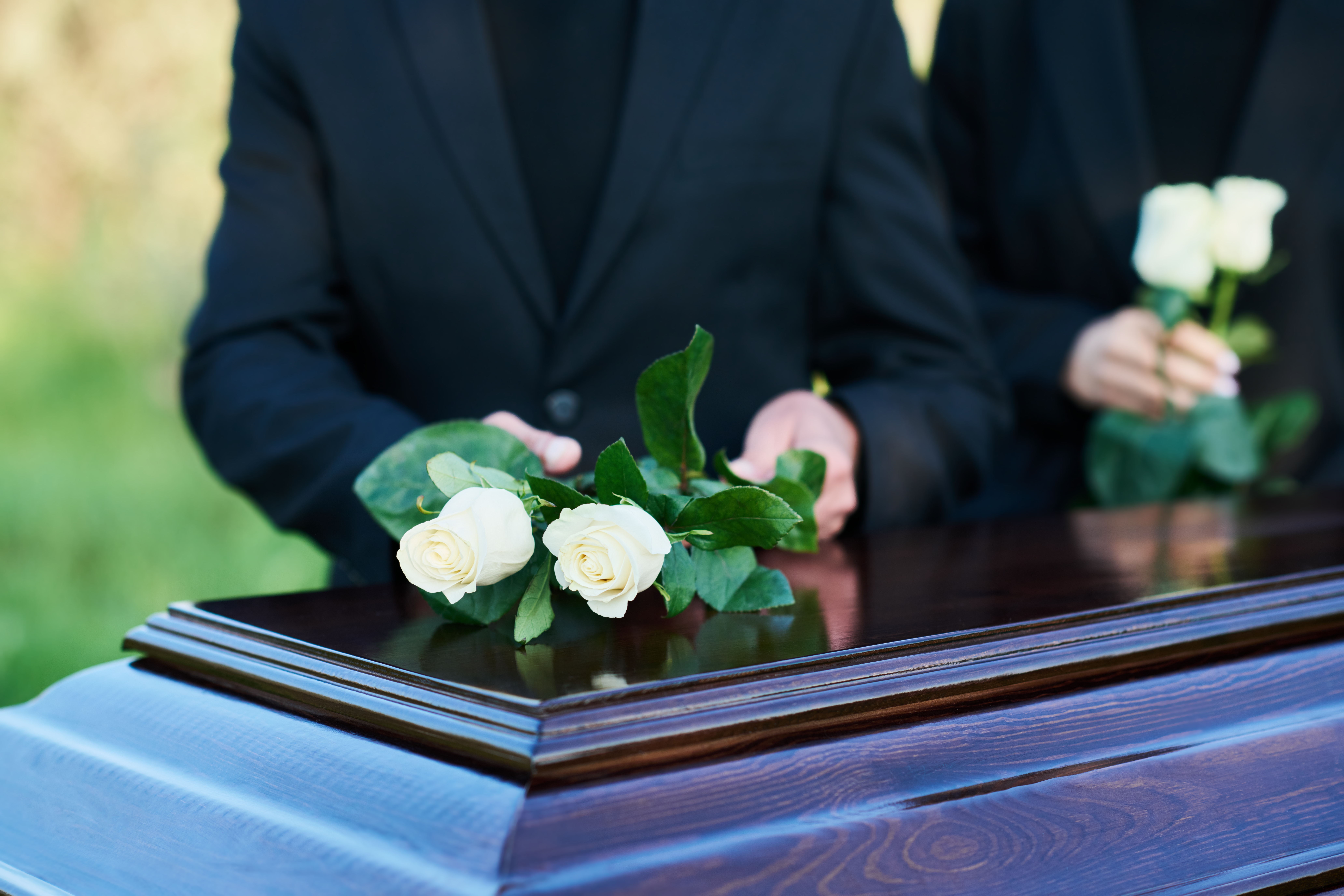 Des personnes déposent des roses blanches sur un cercueil | Source : Shutterstock