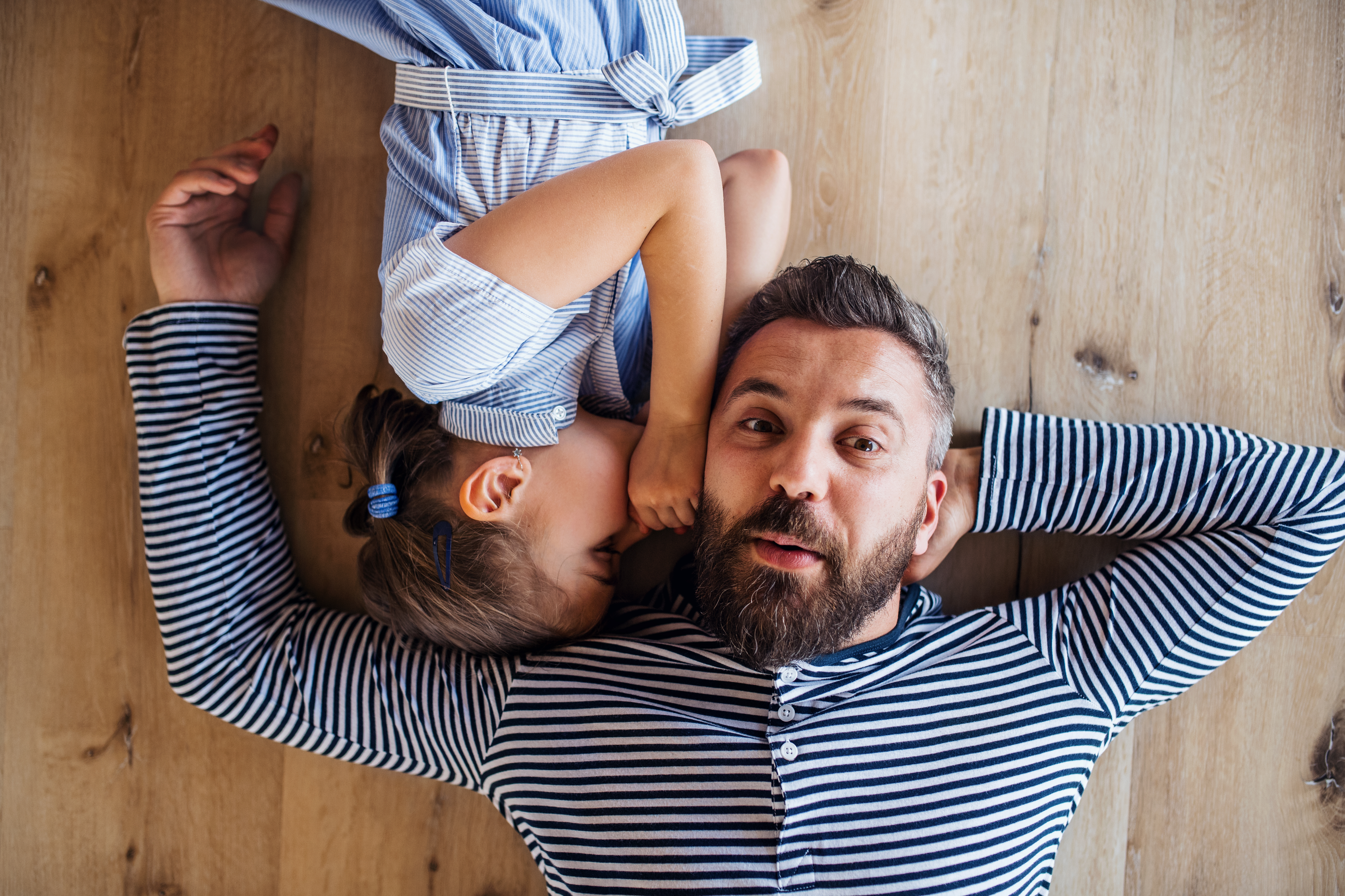 Vue du dessus d'un père d'âge mûr et d'une petite fille allongés sur le sol à l'intérieur de la maison, en train de chuchoter | Source : Getty Images