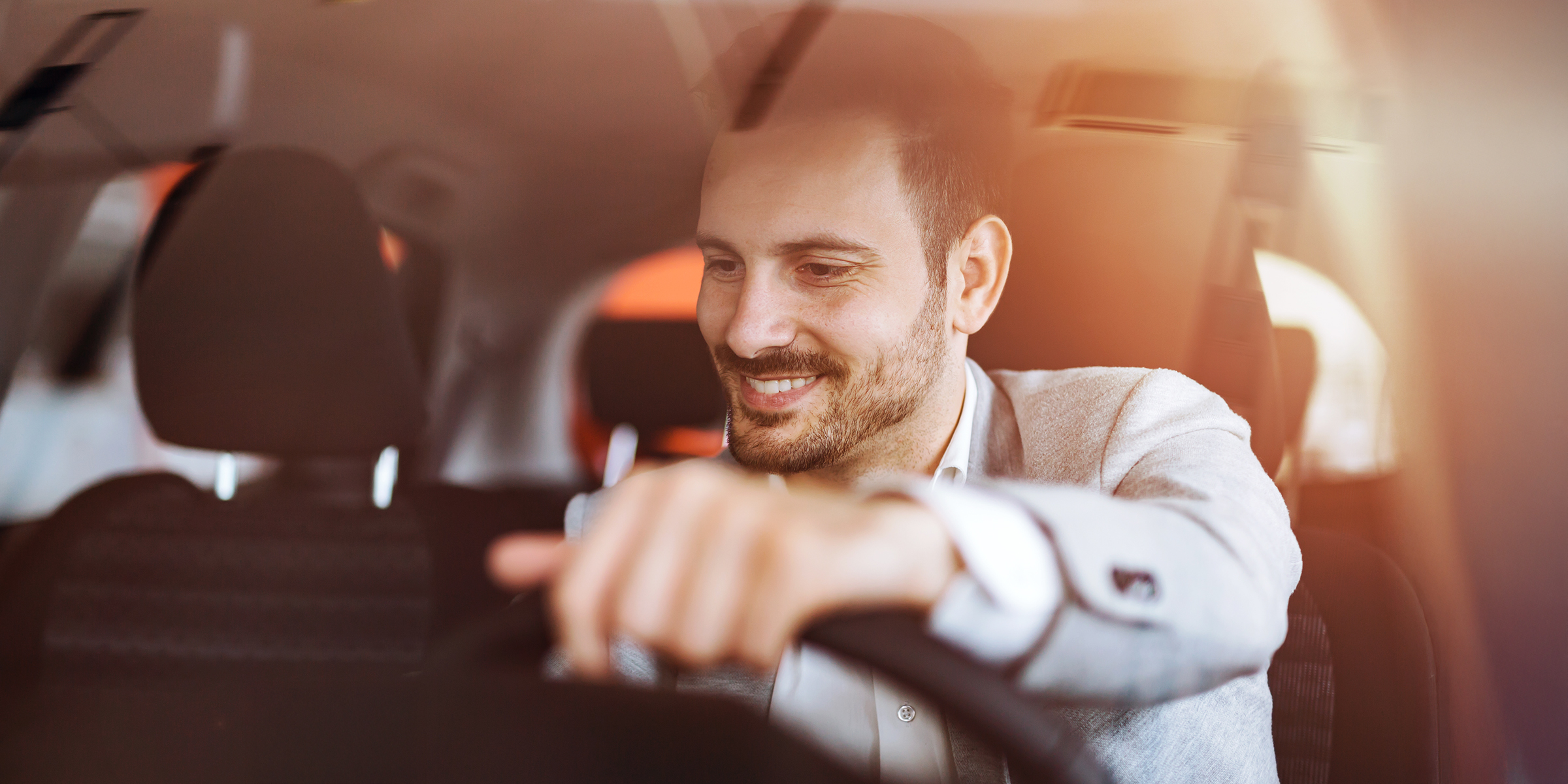 Un homme souriant assis derrière le volant, profitant du trajet dans sa voiture | Source : Shutterstock