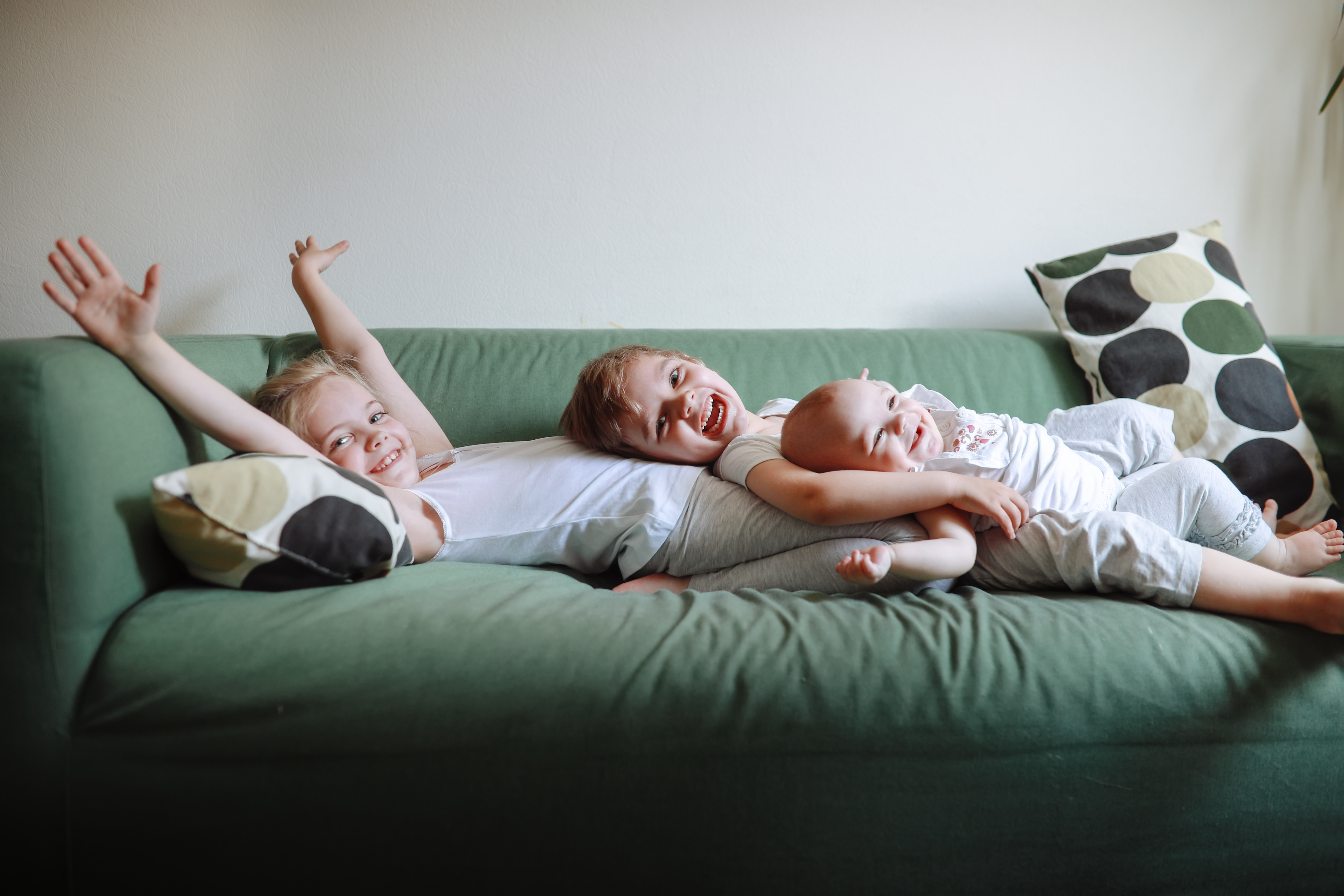 Une sœur et deux petits frères allongés sur un canapé vert | Source : Getty Images