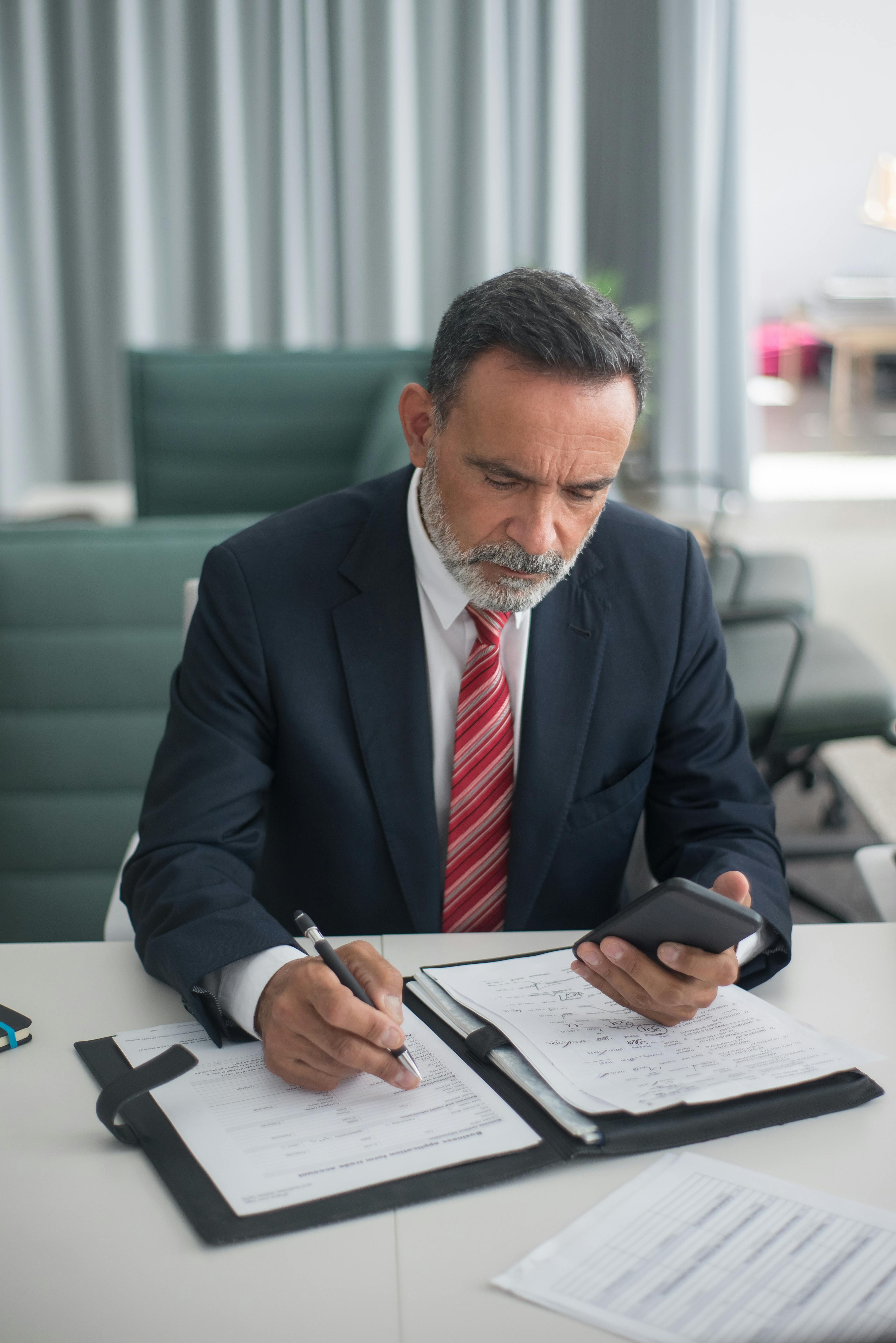 Un homme en costume parcourant des documents administratifs | Source : Pexels