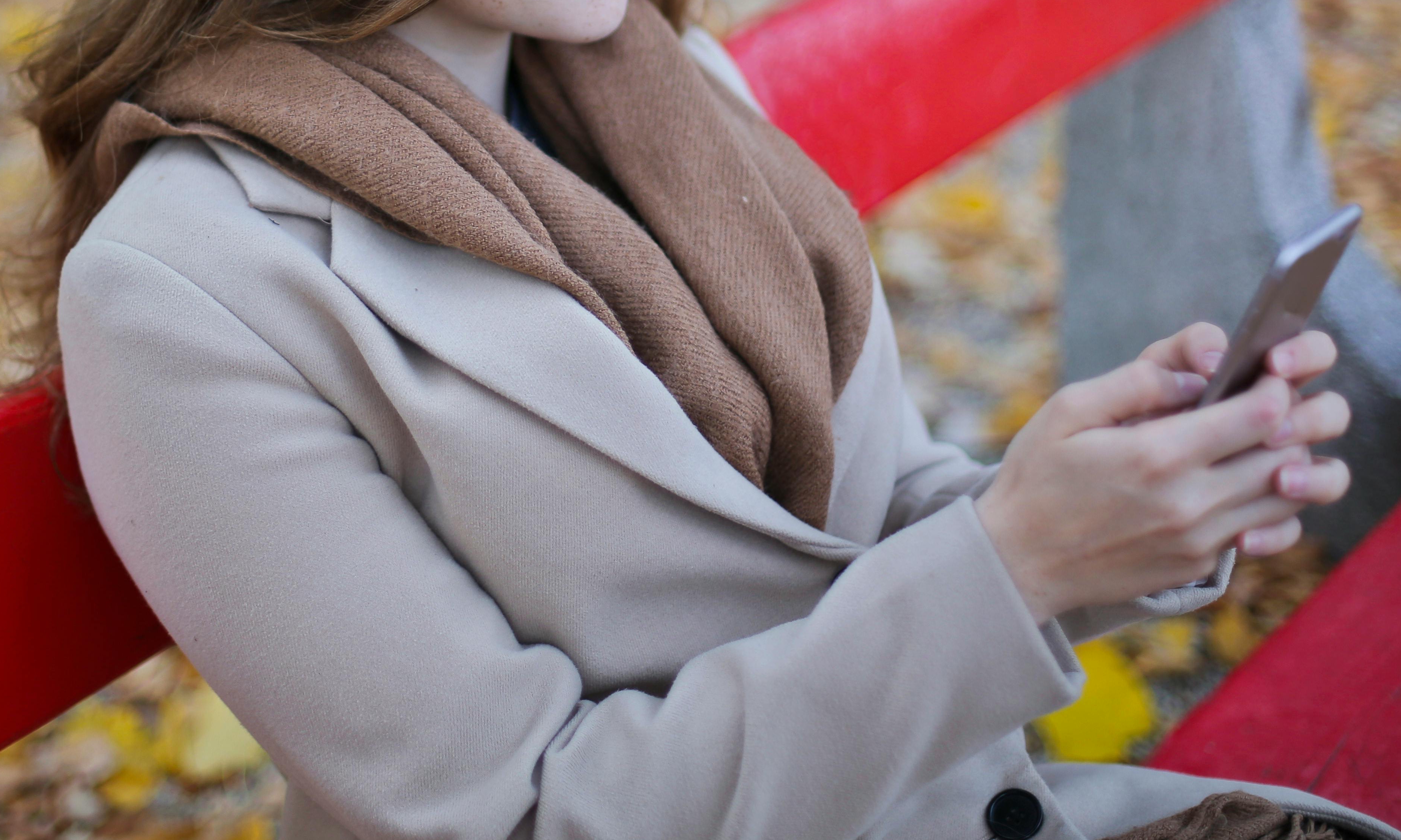 Une femme assise sur un banc public avec un téléphone portable dans les mains | Source : Pexels