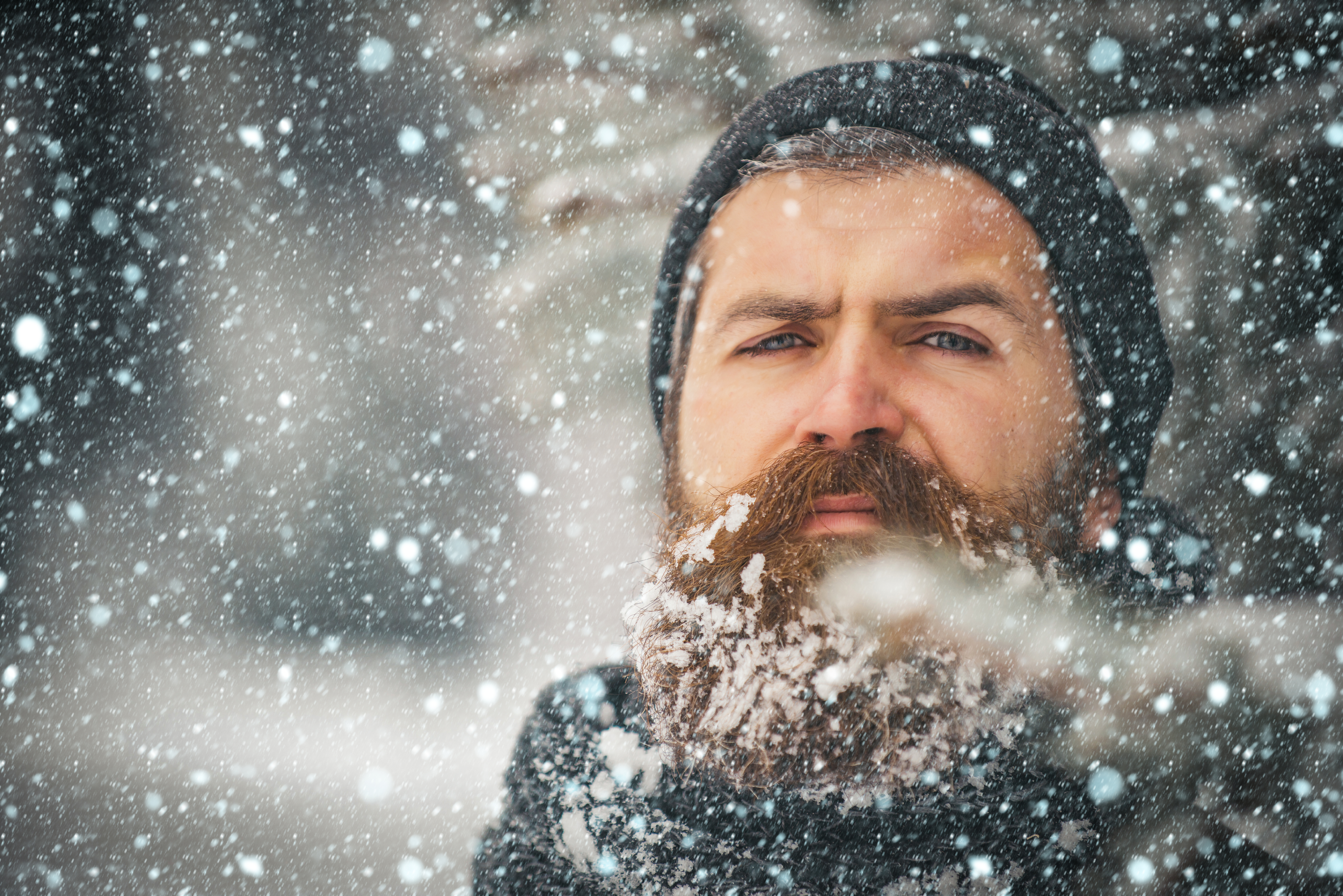 Un homme avec une barbe et un chapeau, debout à l'extérieur alors que la neige tombe | Source : Shutterstock