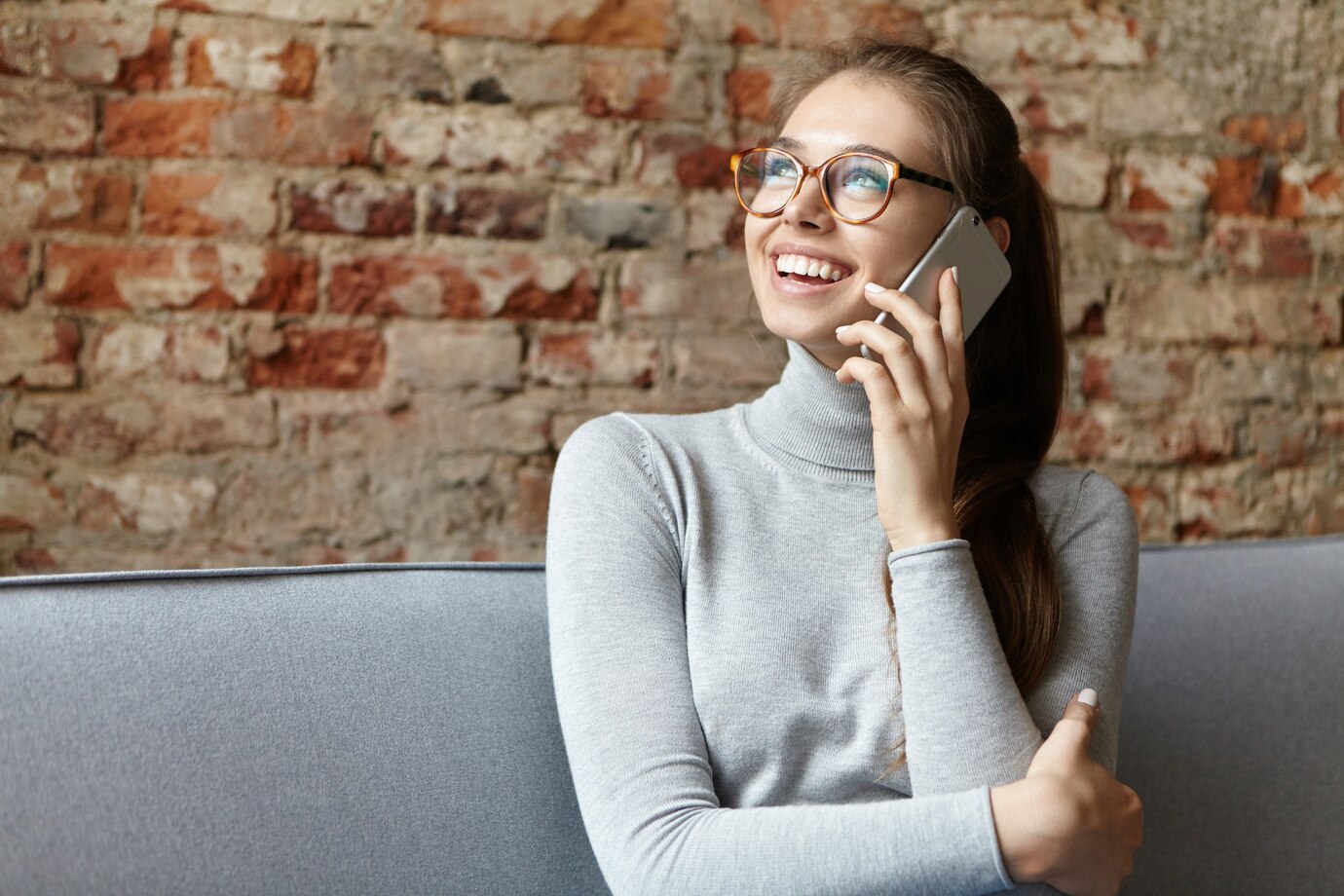 Une femme souriante qui parle au téléphone en regardant vers le haut ⏐ Source : Freepik