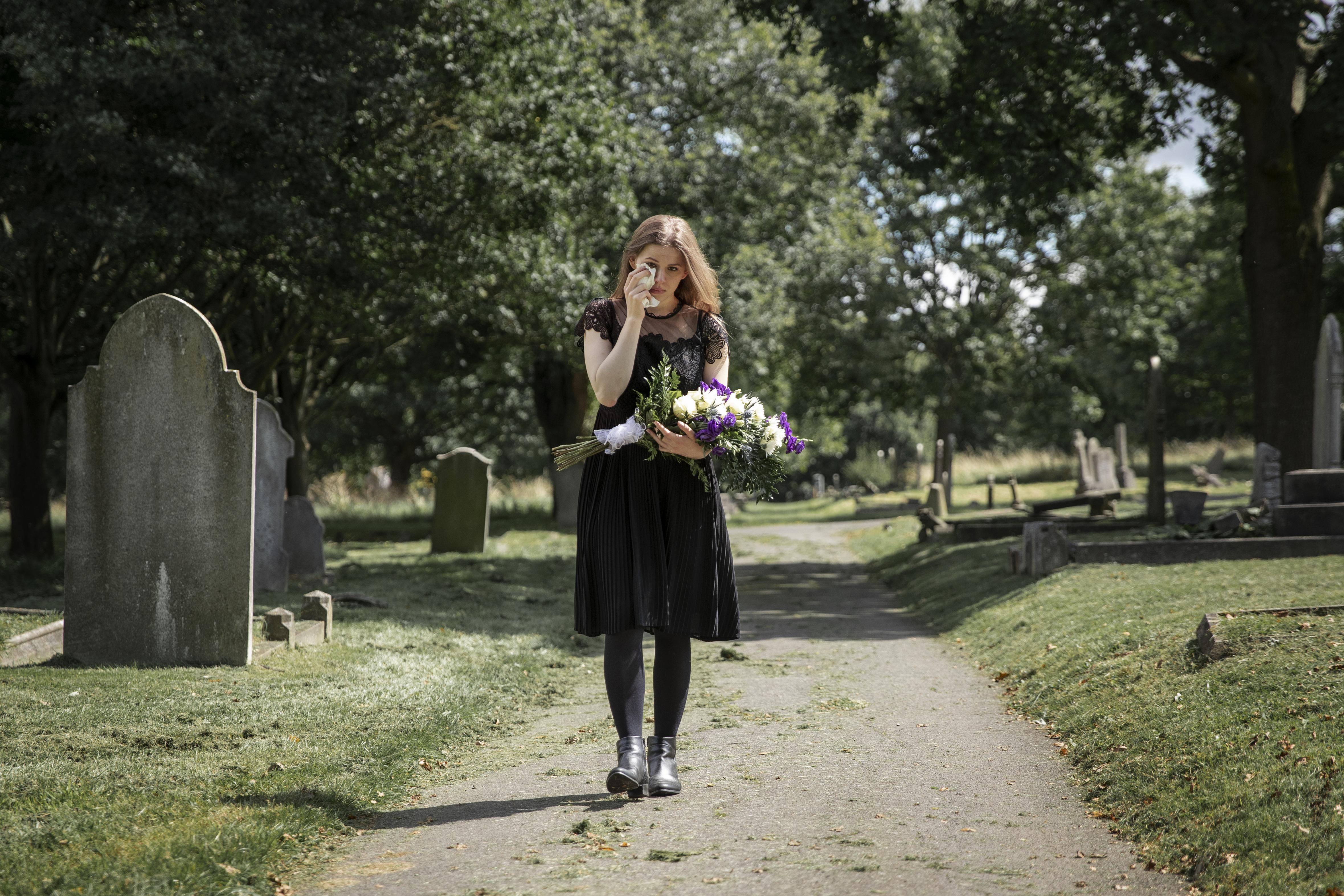 Une femme en deuil tenant un bouquet de fleurs dans un cimetière | Source : Freepik