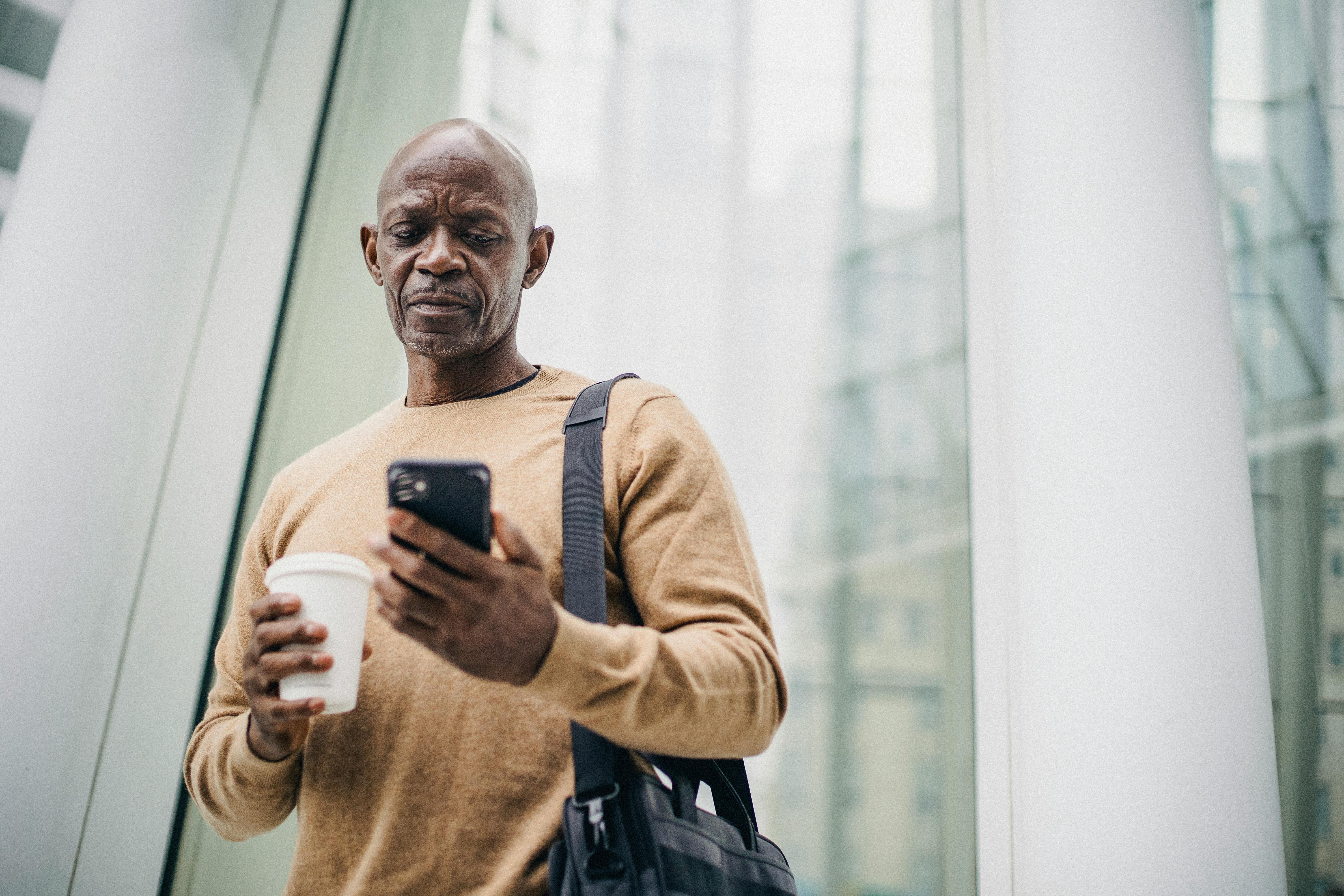 Un homme âgé qui a l'air triste en regardant son téléphone tout en tenant une boisson | Source : Pexels