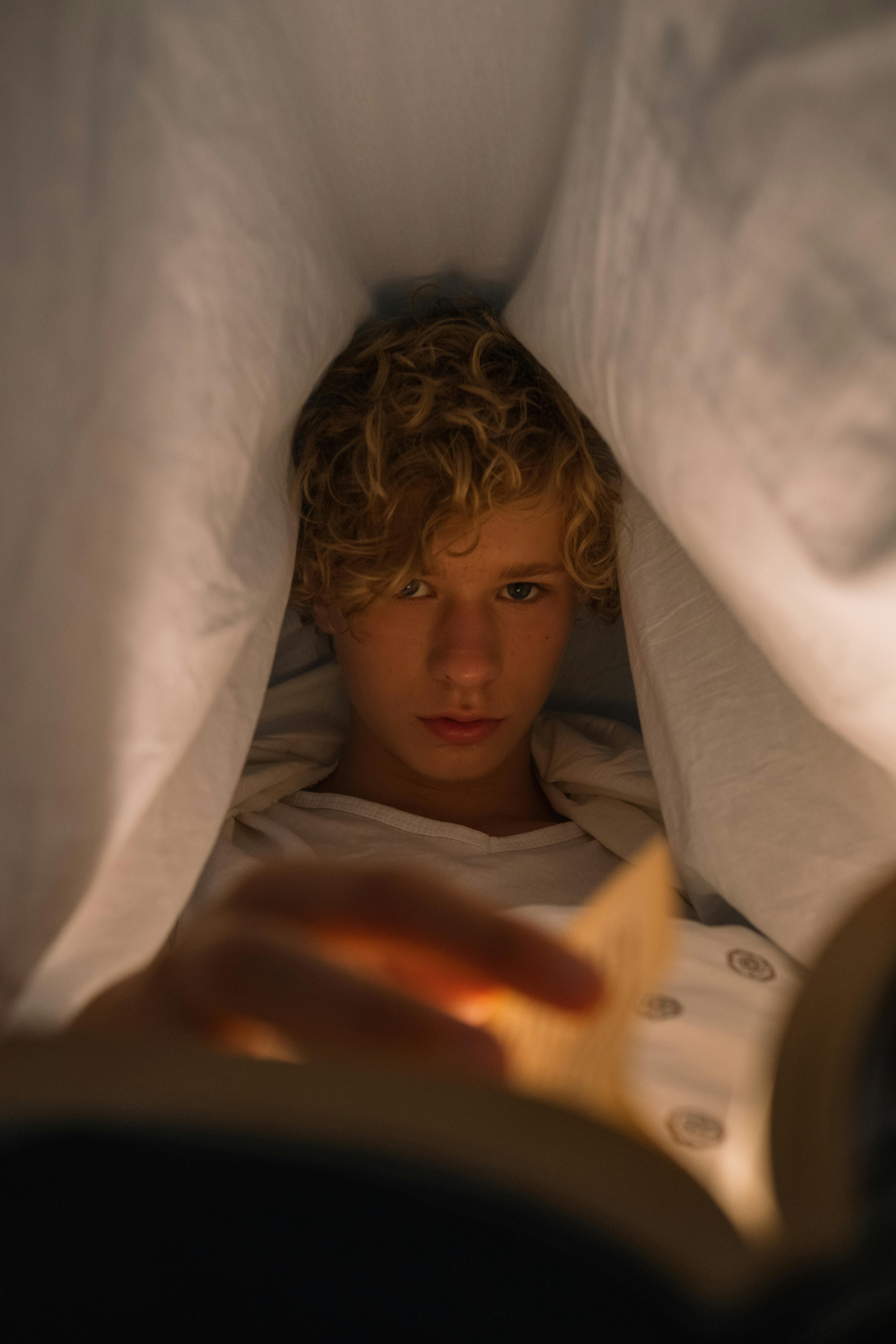 Adolescent lisant sous le drap de lit la nuit | Source : Pexels