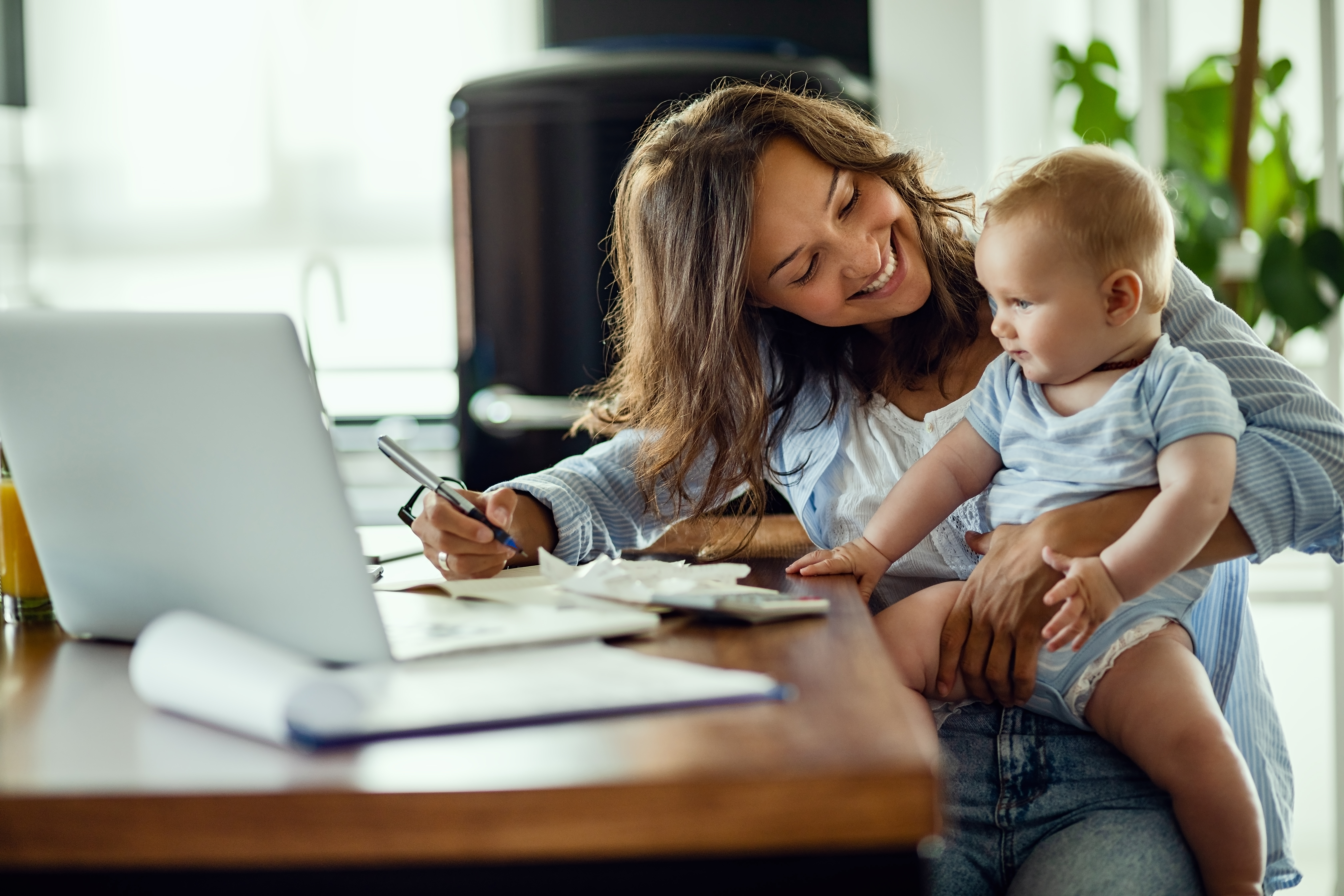 Une femme souriant à son enfant alors qu'elle est assise sur un bureau | Source : Shutterstock