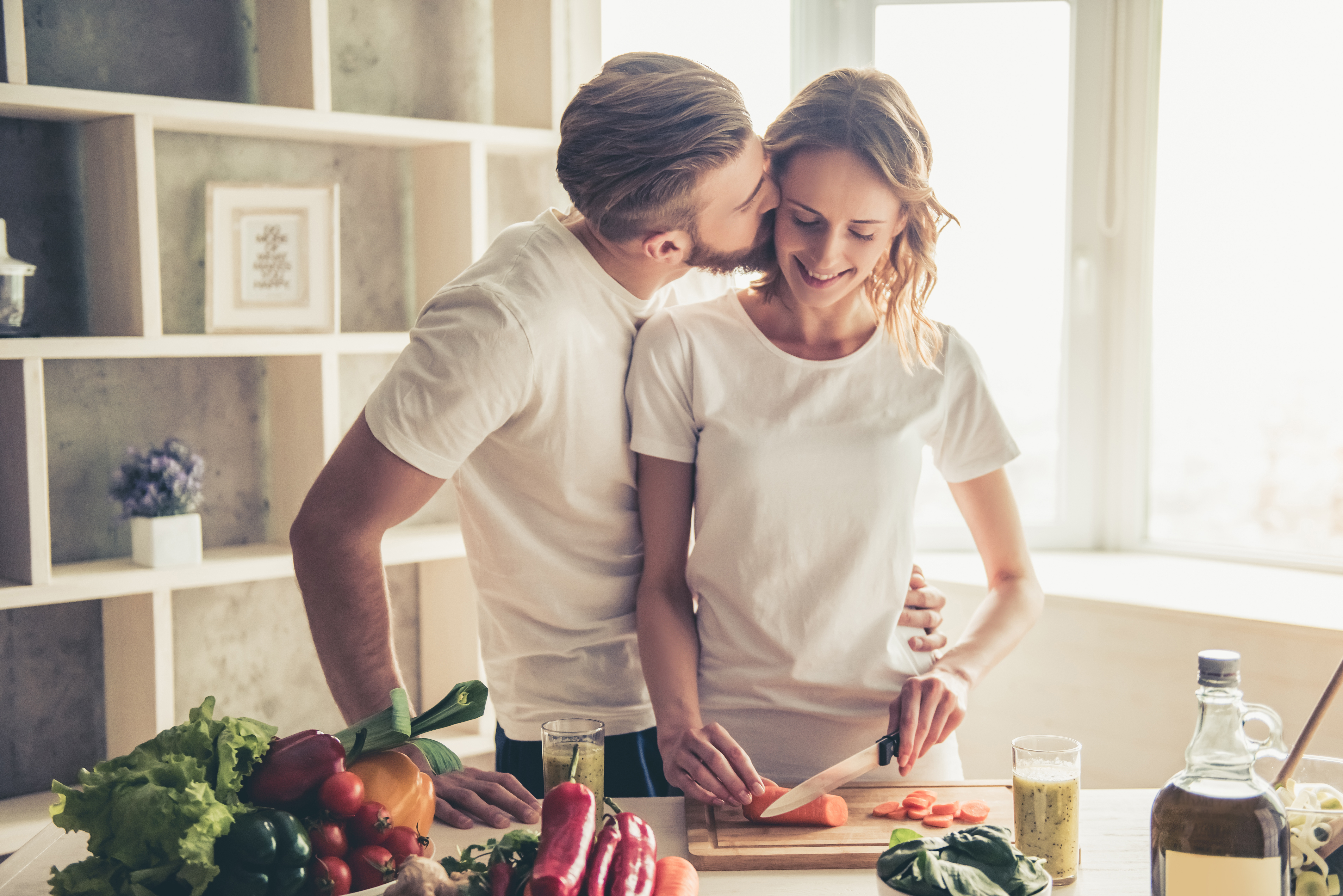 Un homme embrassant sa femme pendant qu'elle coupe des légumes | Source : Shutterstock