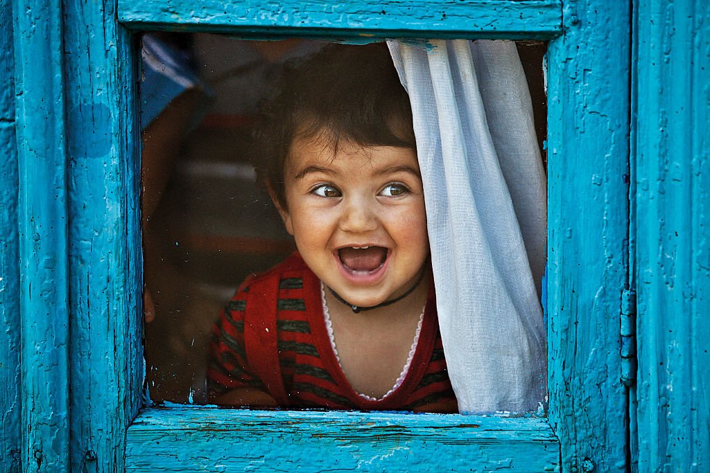 Enfant souriant à travers la fenêtre | Getty Images
