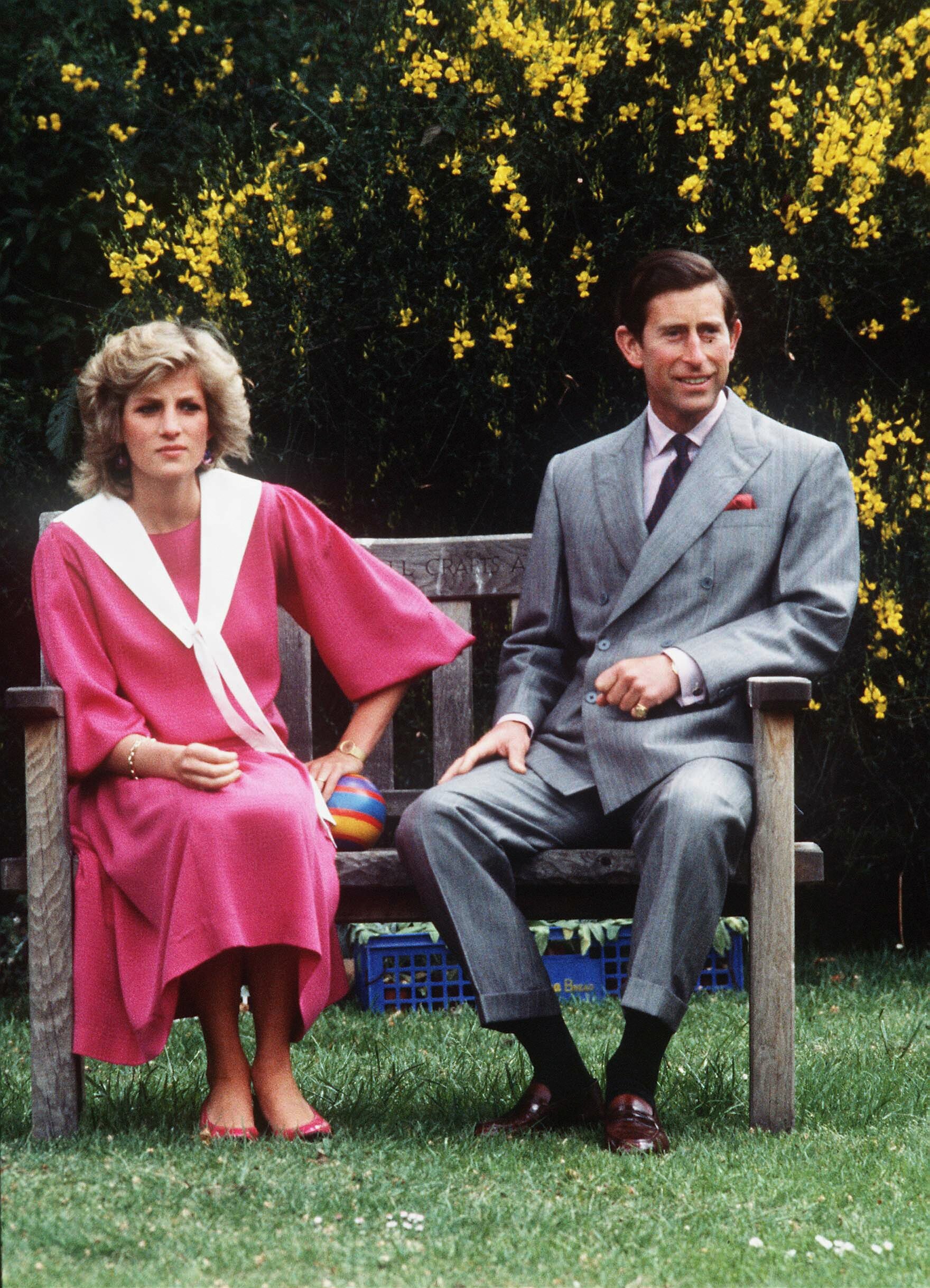 Le Prince Charles et la Princesse Diana, enceinte de 6 mois du Prince Harry, assis sur un banc en bois lors d'un photocall dans le jardin de leur maison à Kensington Palace le 12 juin 1984 à Londres, Royaume-Uni. / Source : Getty Images