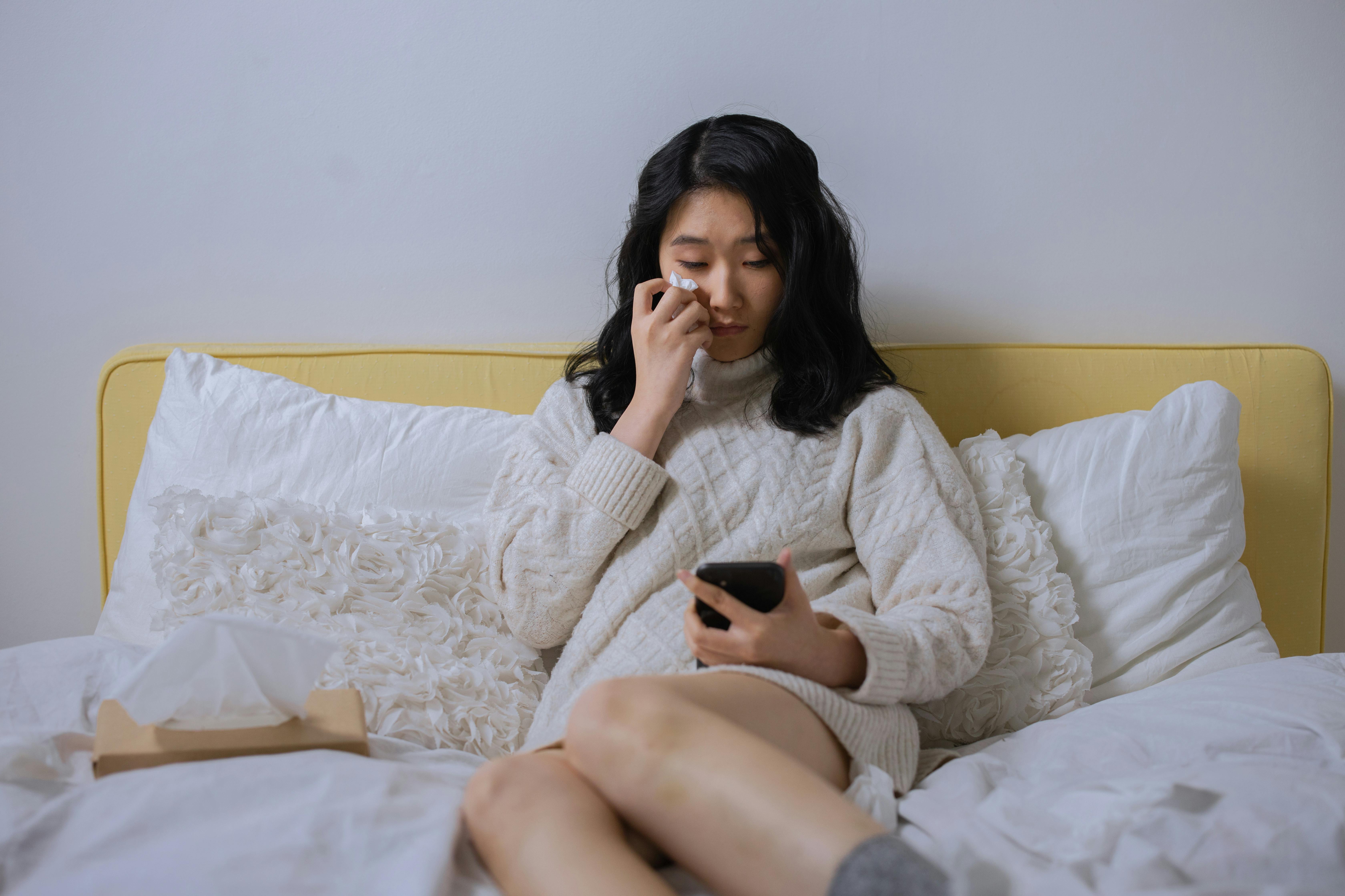 Une femme qui pleure et essuie ses larmes en tenant un téléphone dans son lit | Source : Pexels
