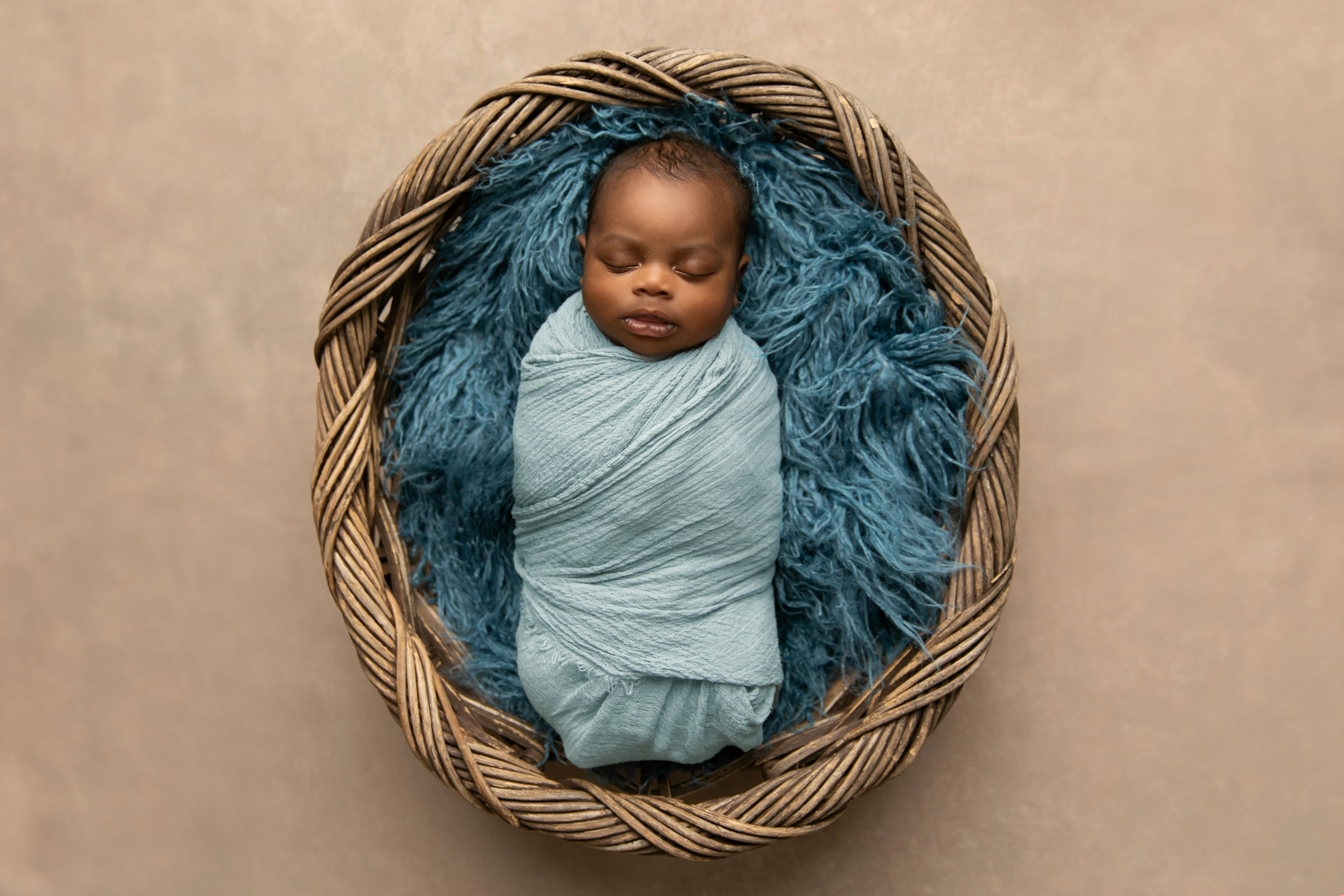 Un nouveau-né afro-américain posé sur un tapis bleu dans un panier et emmailloté dans une couverture | Source : Shutterstock