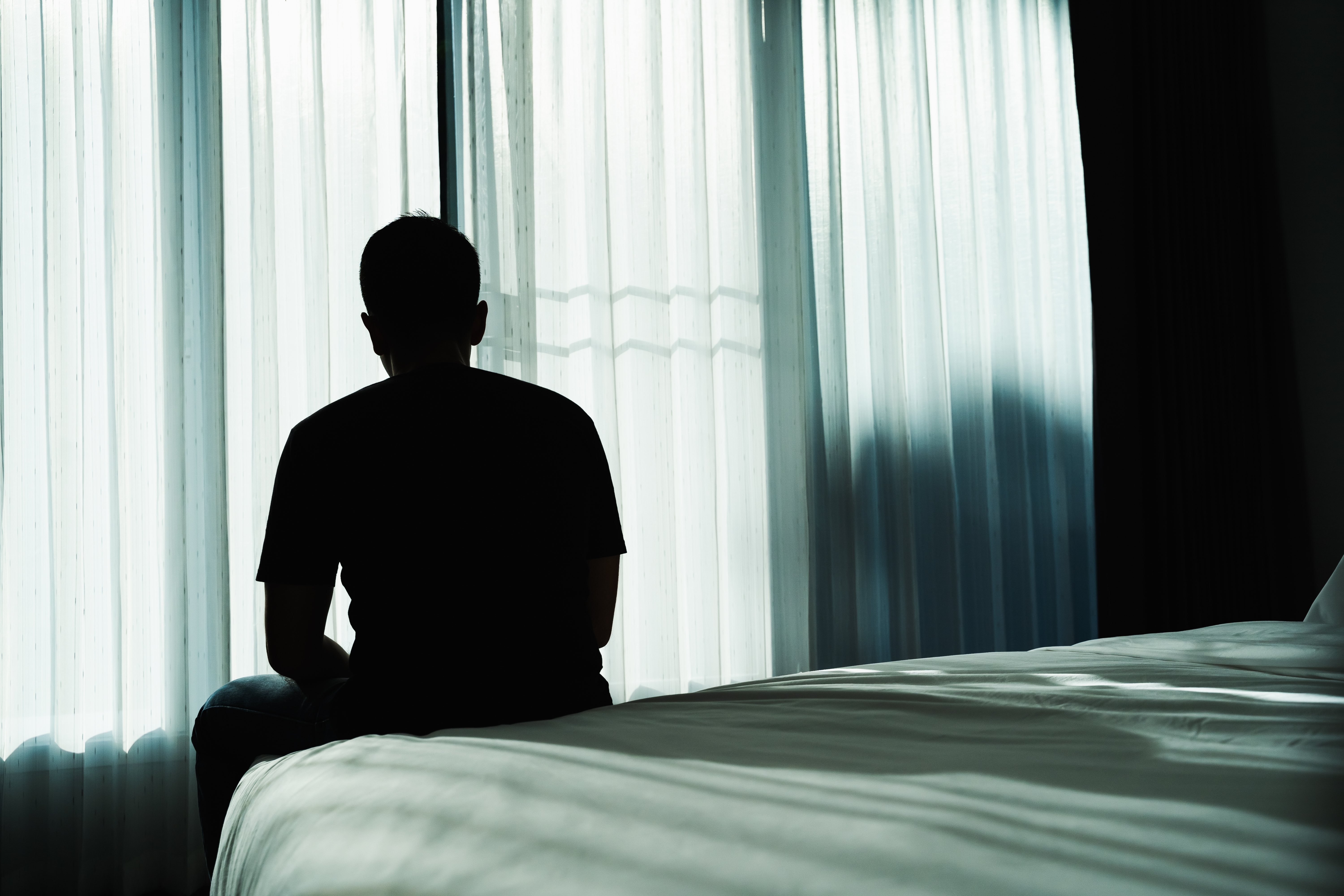 Silhouette d'un homme assis sur un lit | Source : Shutterstock