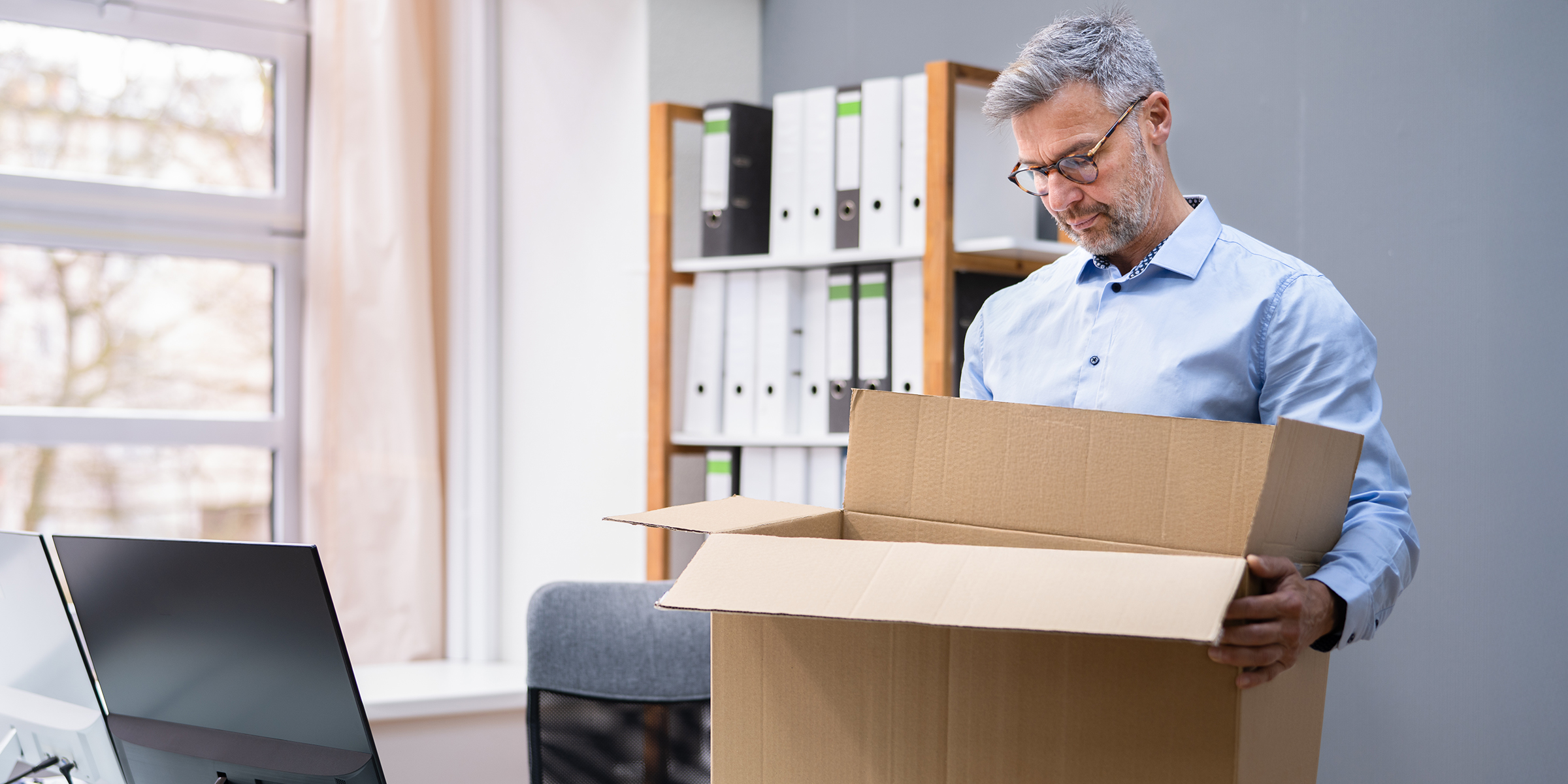 Un homme debout dans son bureau et regardant une boîte en carton ouverte alors qu'il emballe ses affaires | Source : Shutterstock