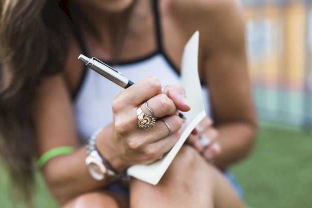 Une femme exhibant ses bagues tout en écrivant dans un carnet de notes. | Photo : Freepik