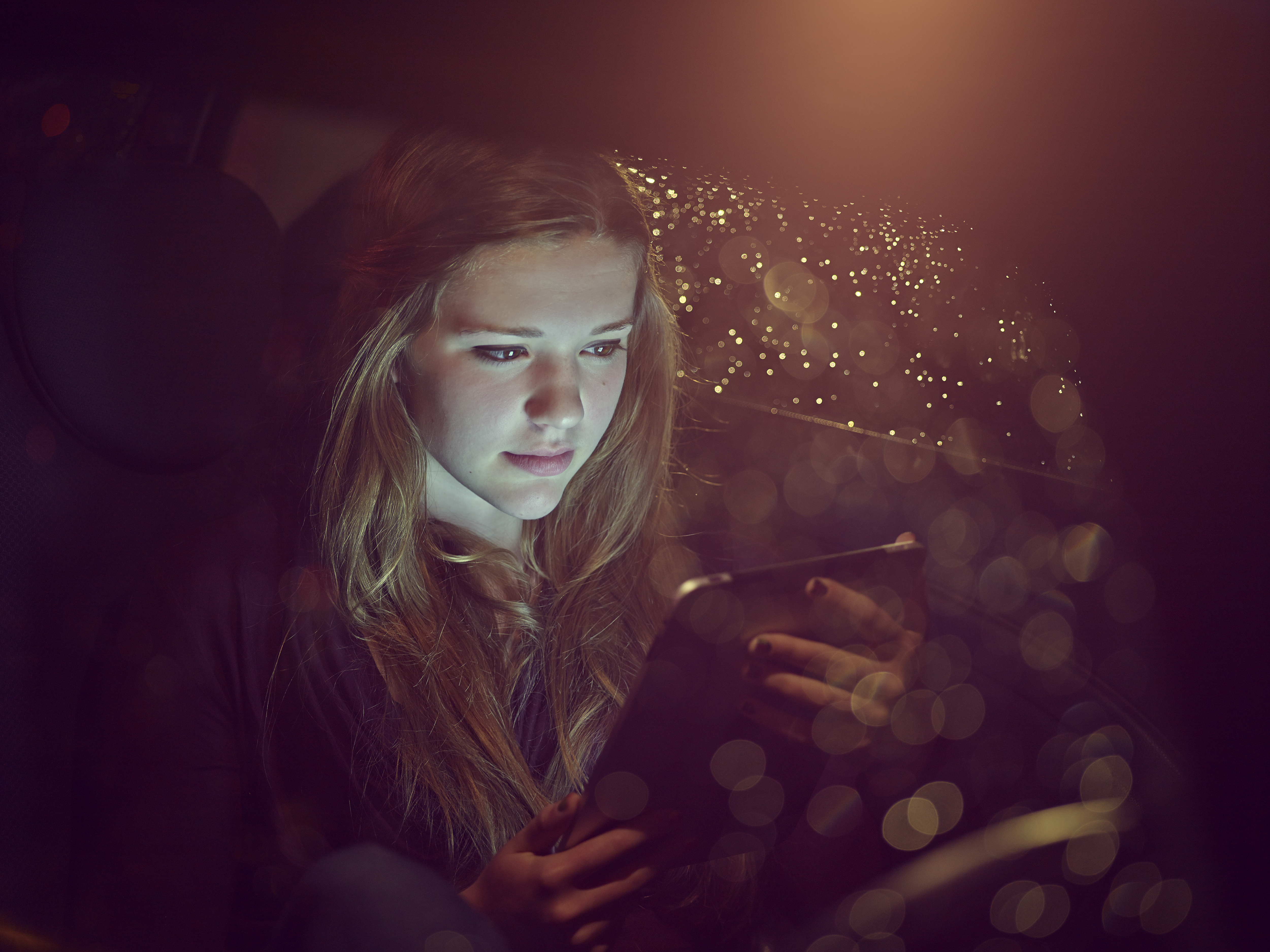Adolescente sur une tablette électronique dans une voiture la nuit | Source : Getty Images