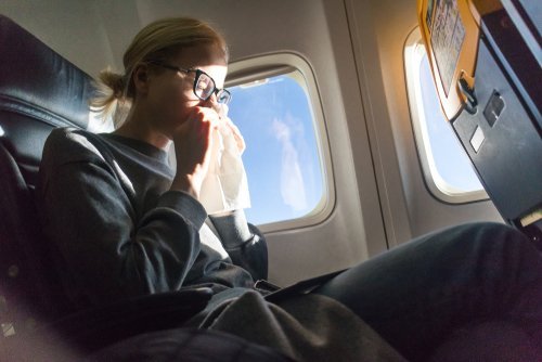 Une jeune femme éternuant dans un avion | Photo : Shutterstock