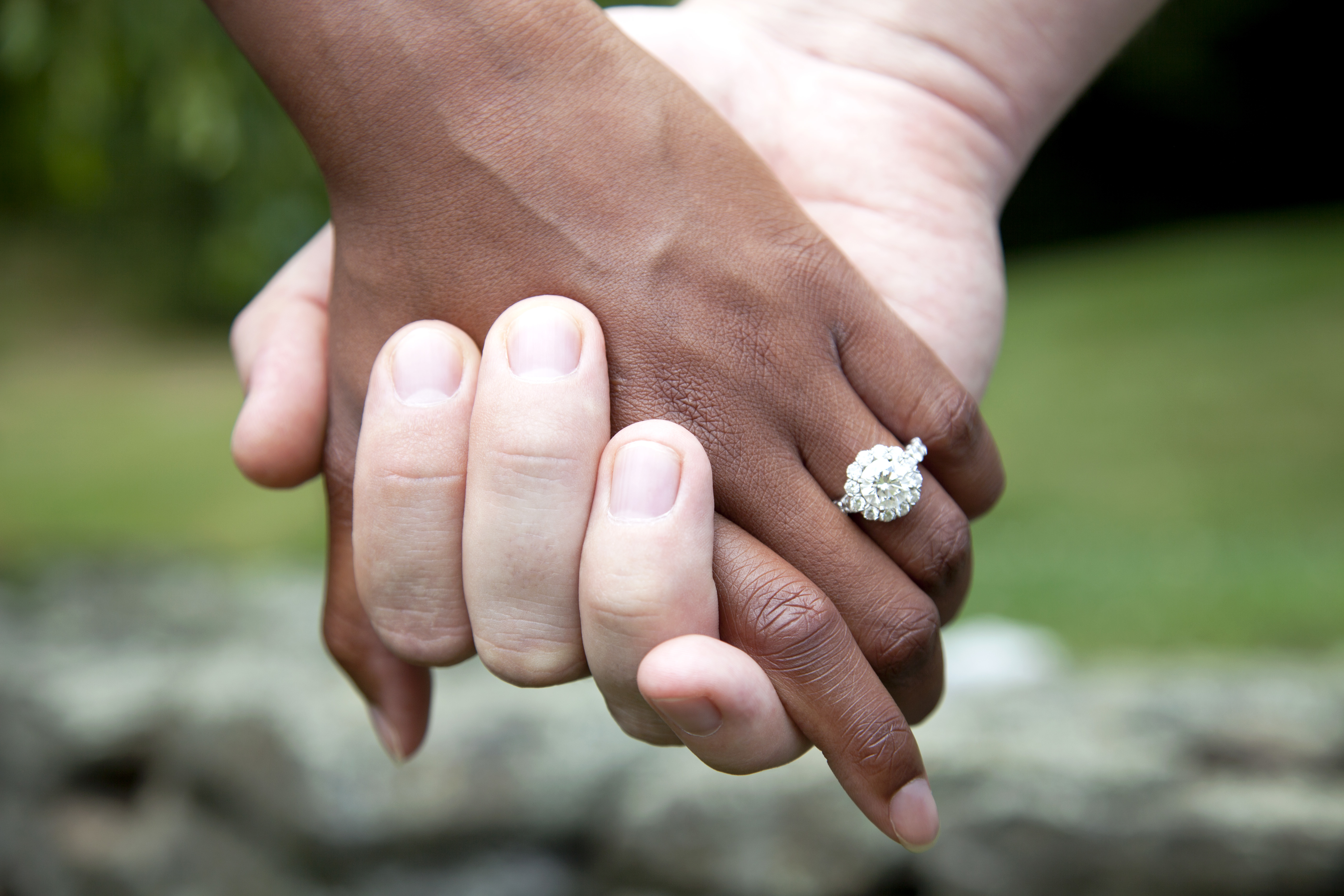 Couple interracial se tenant par la main et bague de fiançailles en diamant, gros plan | Source : Getty Images