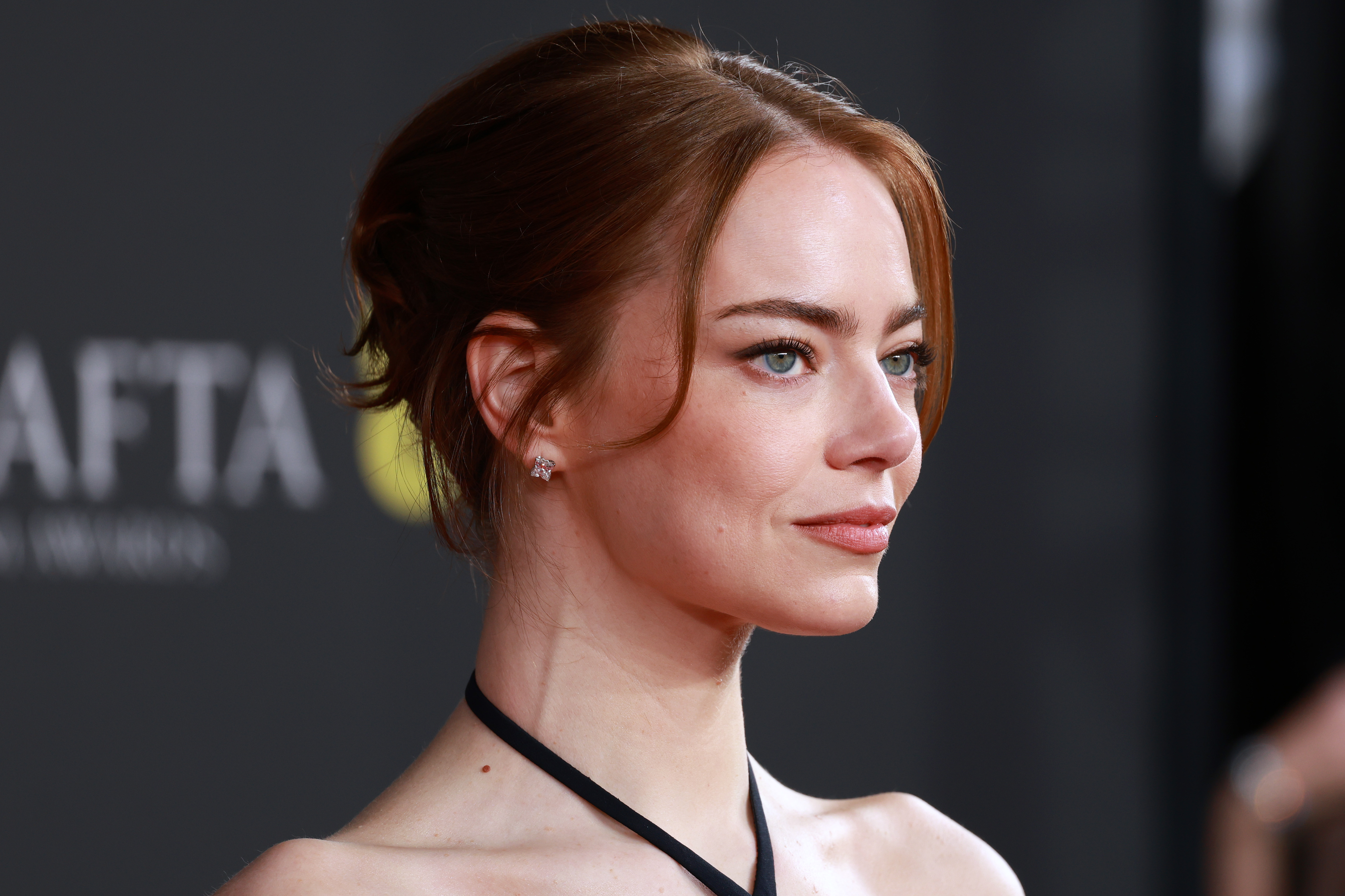 Emma Stone est ravissante dans une élégante robe noire dos nu, avec ses cheveux auburn coiffés en chignon et ses délicates boucles d'oreilles en diamant qui ajoutent une touche raffinée à son décolleté audacieux et ses épaules sculptées.