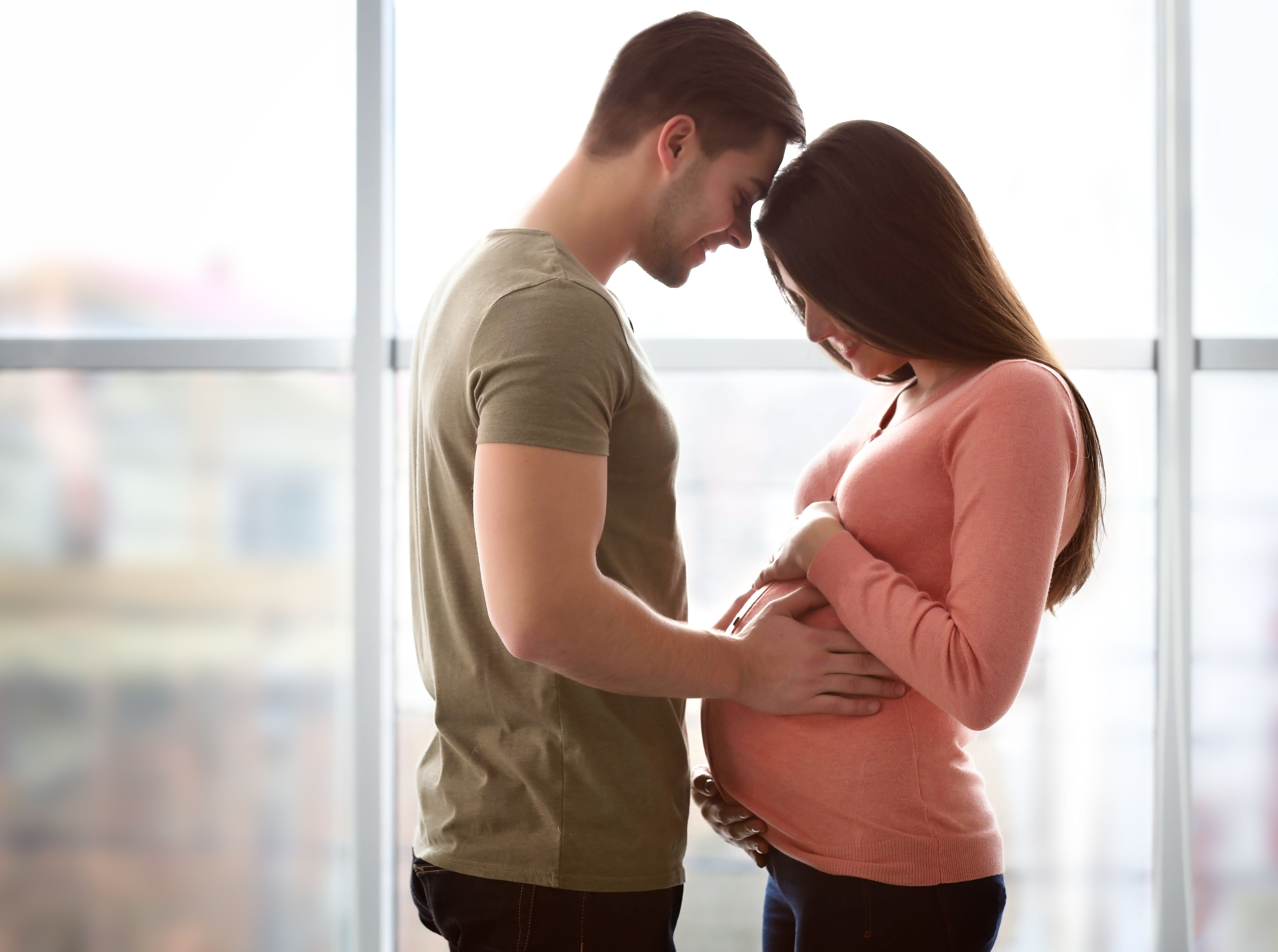 Une femme regarde son ventre de femme enceinte tandis que son mari pose son front sur le sien | Source : Shutterstock