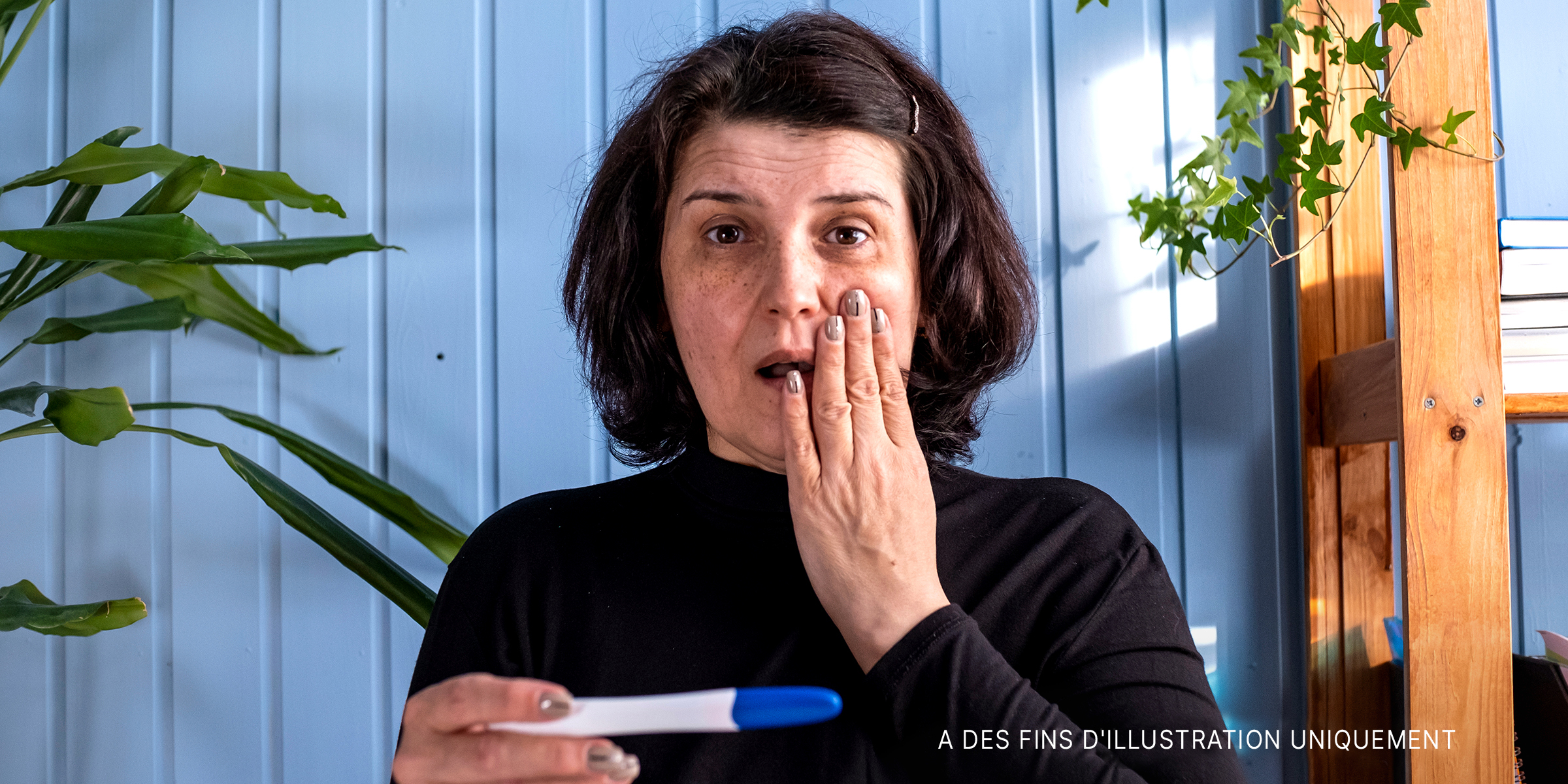 Une femme d'âge moyen regarde le résultat d'un test de grossesse qui s'avère positif | Source : Shutterstock
