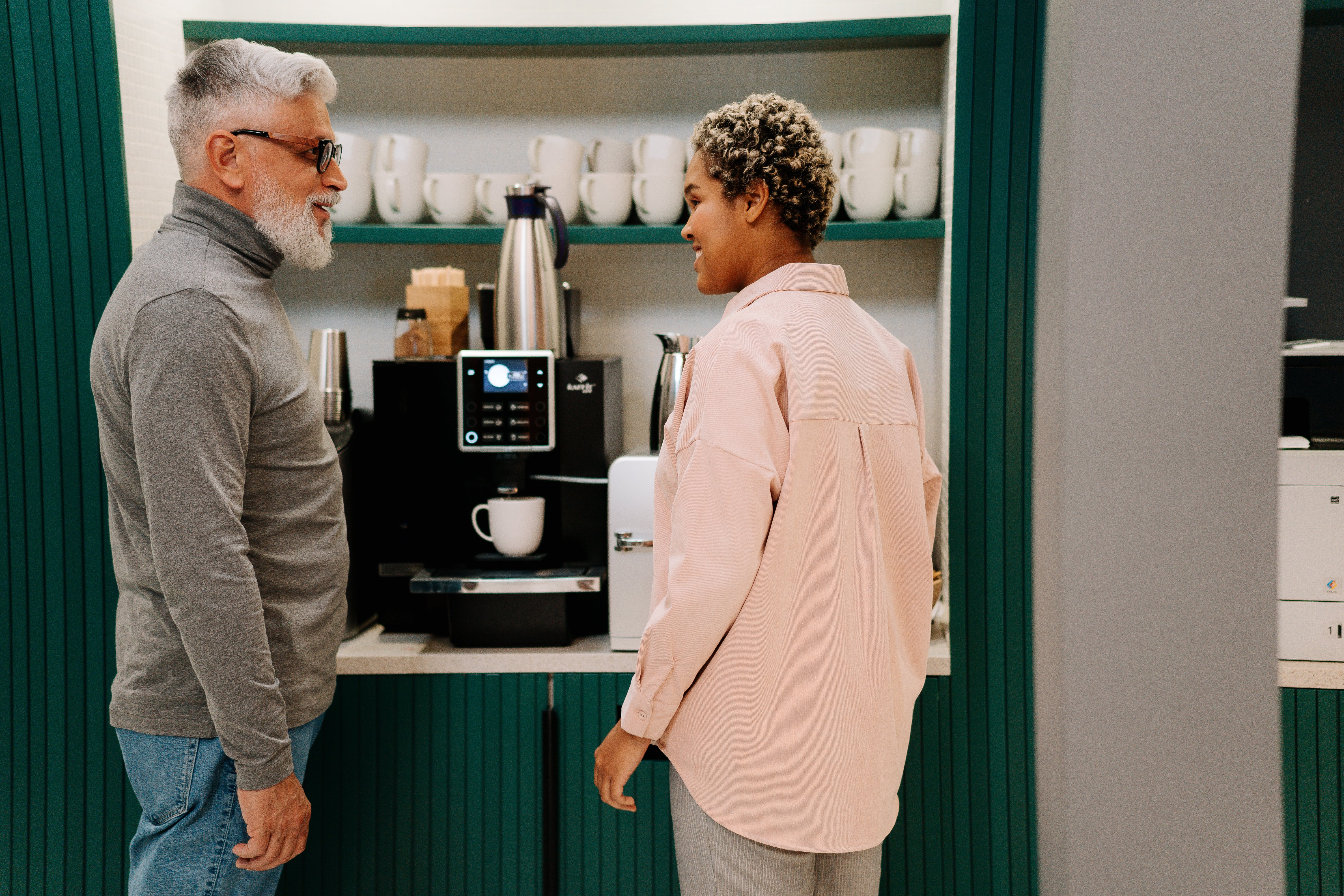 Un homme plus âgé parle à une femme plus jeune tout en se tenant devant une machine à café | Source : Pexels