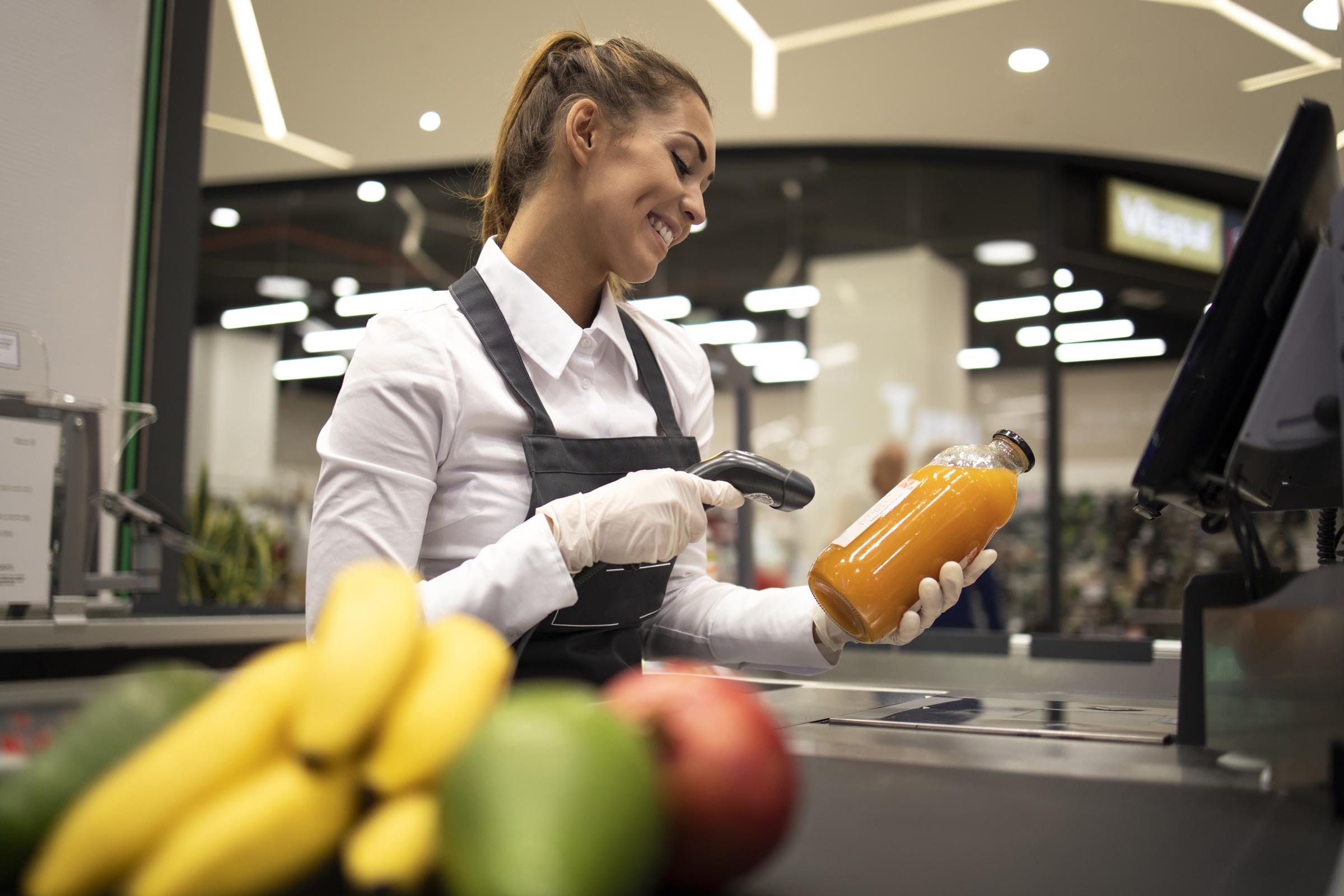 Portrait d'une caissière dans un supermarché en train de scanner les codes-barres des produits à vendre | Source : Magnific