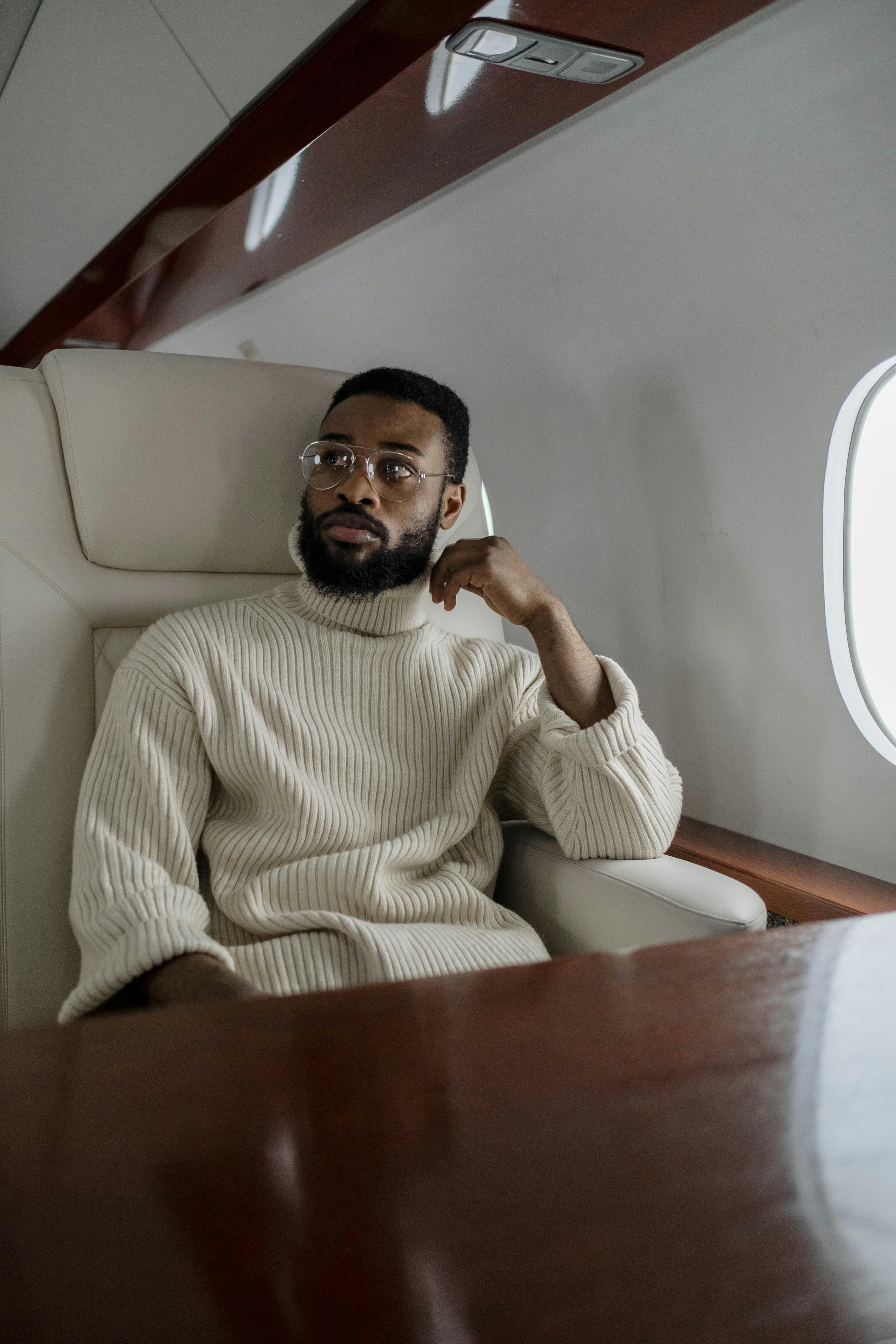 Un homme en pull beige à col roulé à l'intérieur d'un avion | Source : Pexels