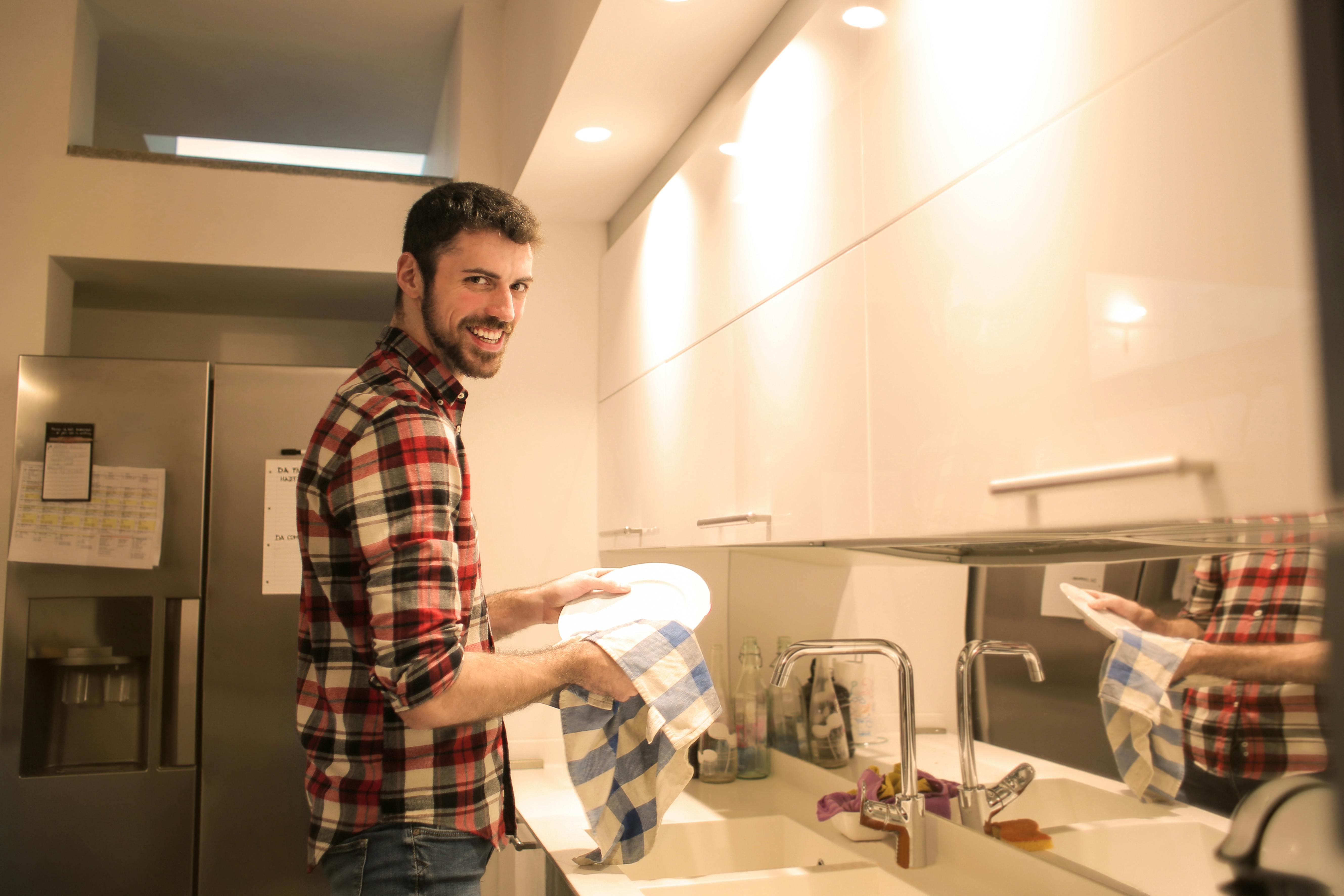 Homme souriant en faisant la vaisselle | Source : Pexels