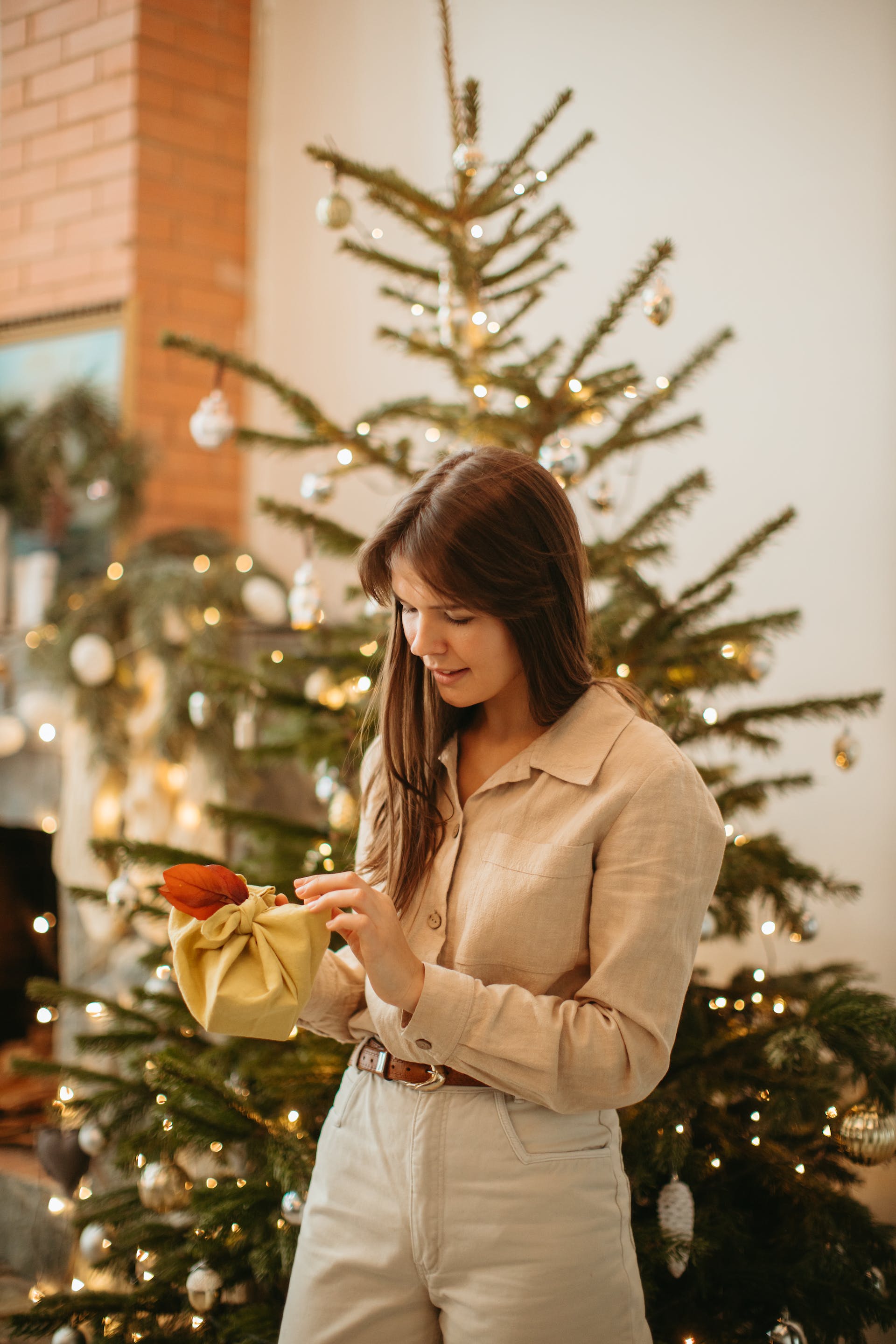 Une femme tient un paquet cadeau alors qu'elle se tient près d'un arbre de Noël | Source : Pexels