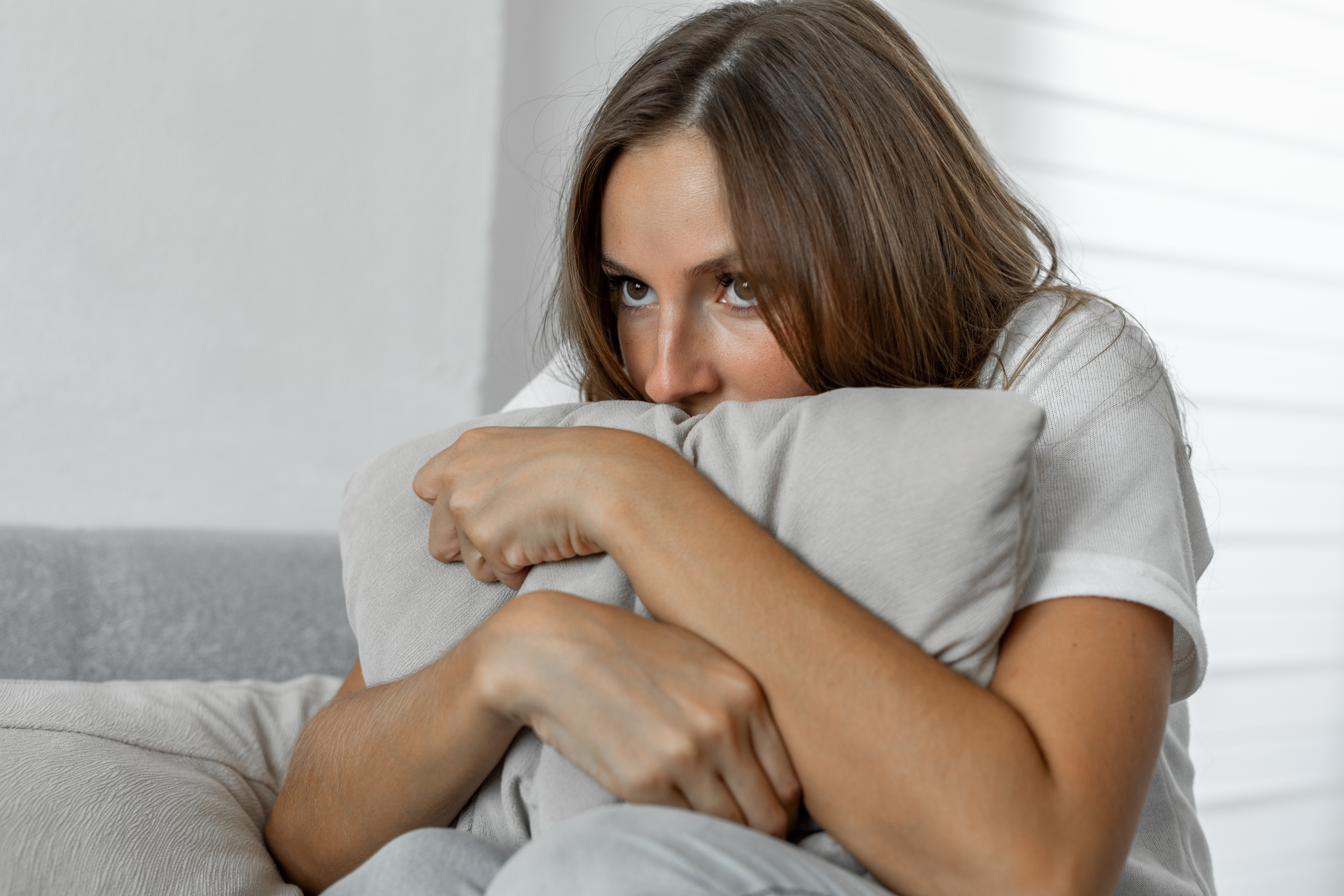 Femme effrayée à la maison embrassant un oreiller assis sur un canapé | Source : Getty Images
