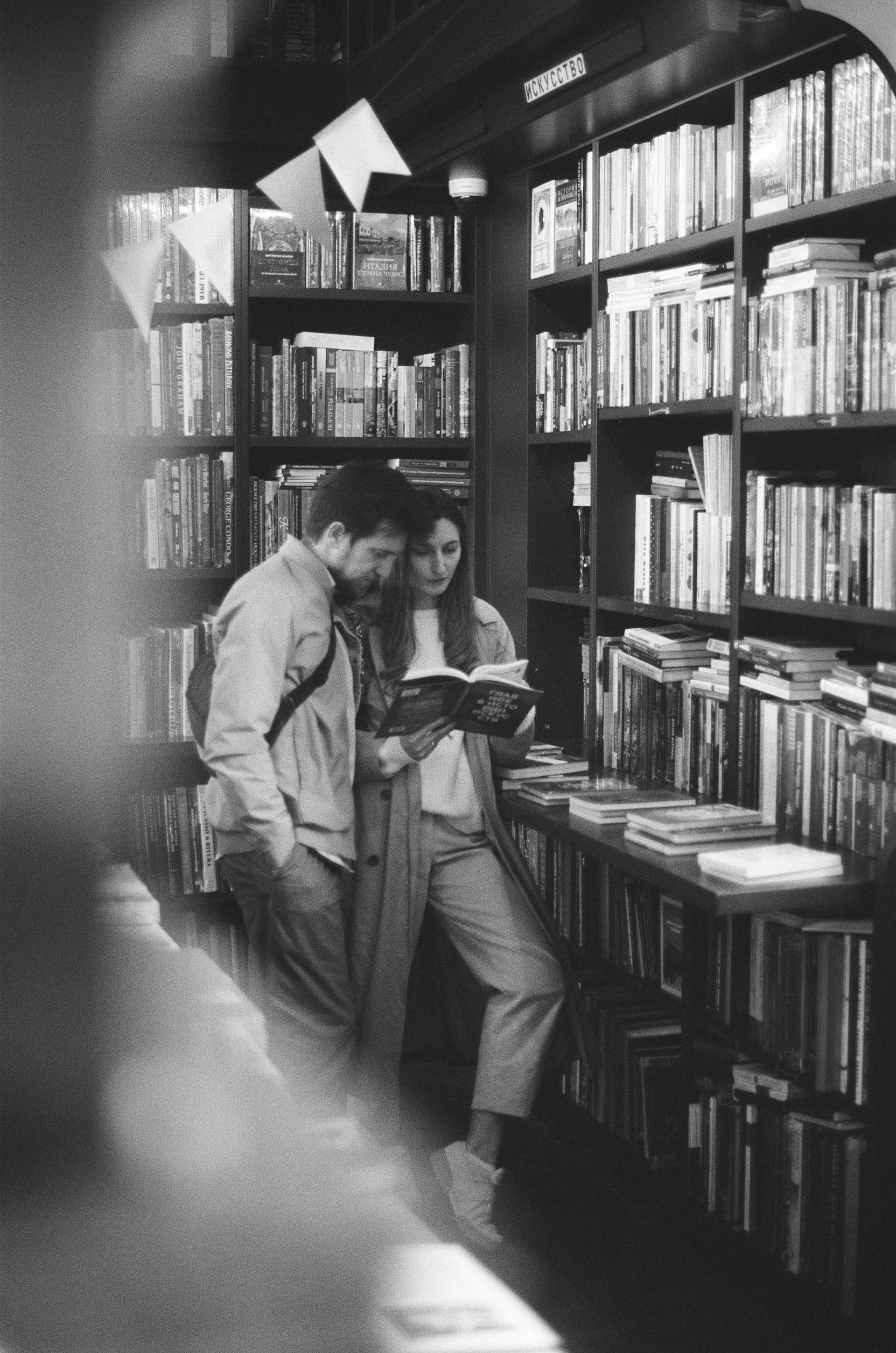 Photo d'un couple lisant un livre dans une bibliothèque | Source : Pexels