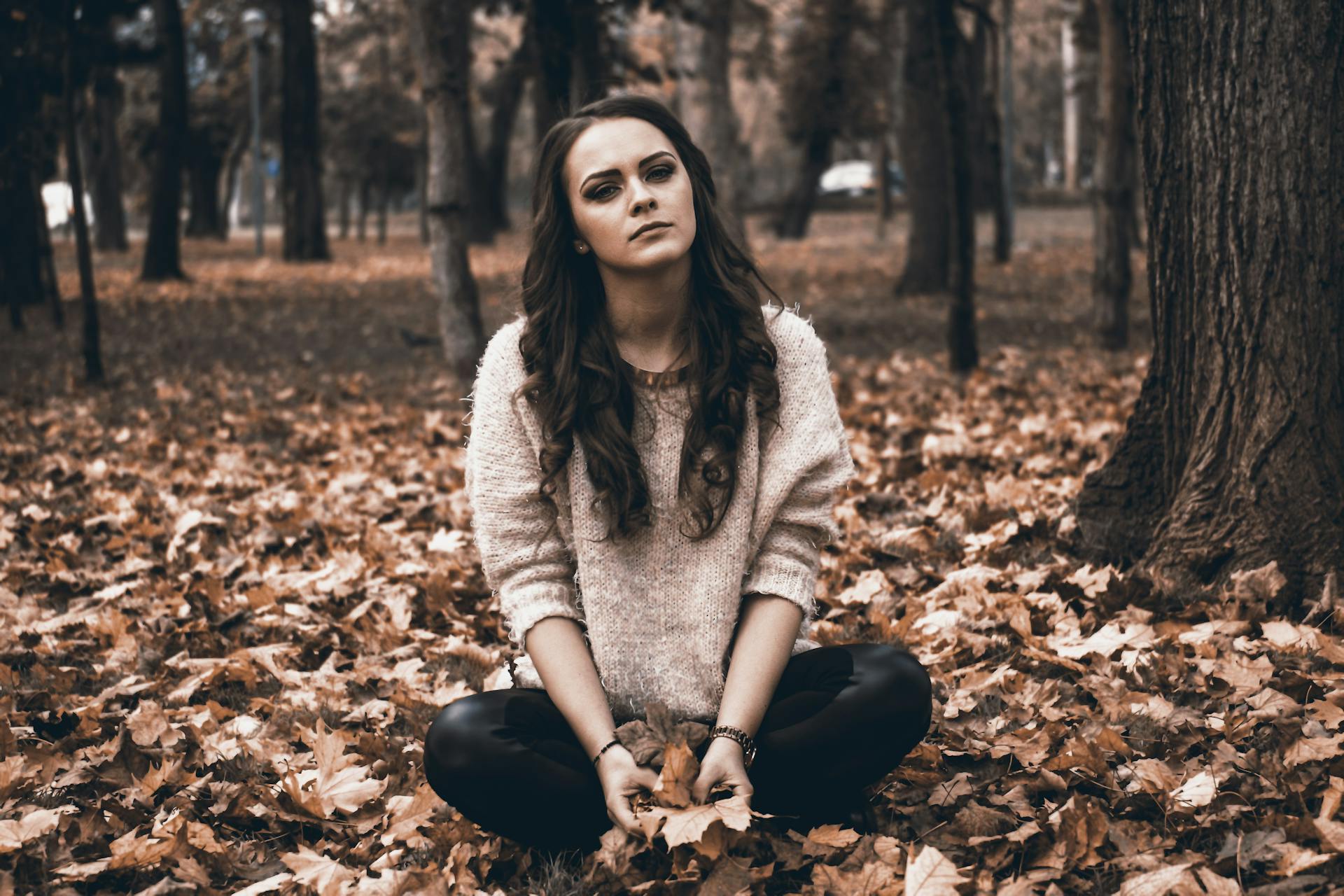 Une jeune femme assise dans une forêt tenant des feuilles mortes | Source : Pexels