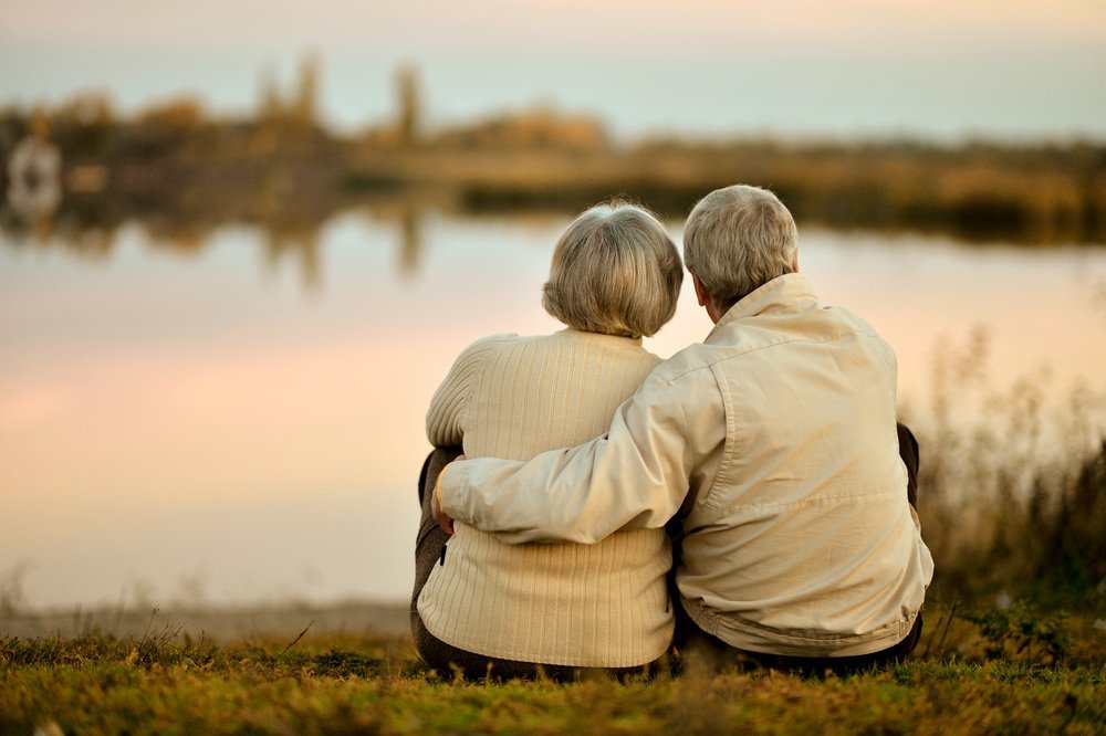 Couple heureux de personnes âgées assis au bord du lac pendant l'été, au coucher du soleil. | Source : Shutterstock