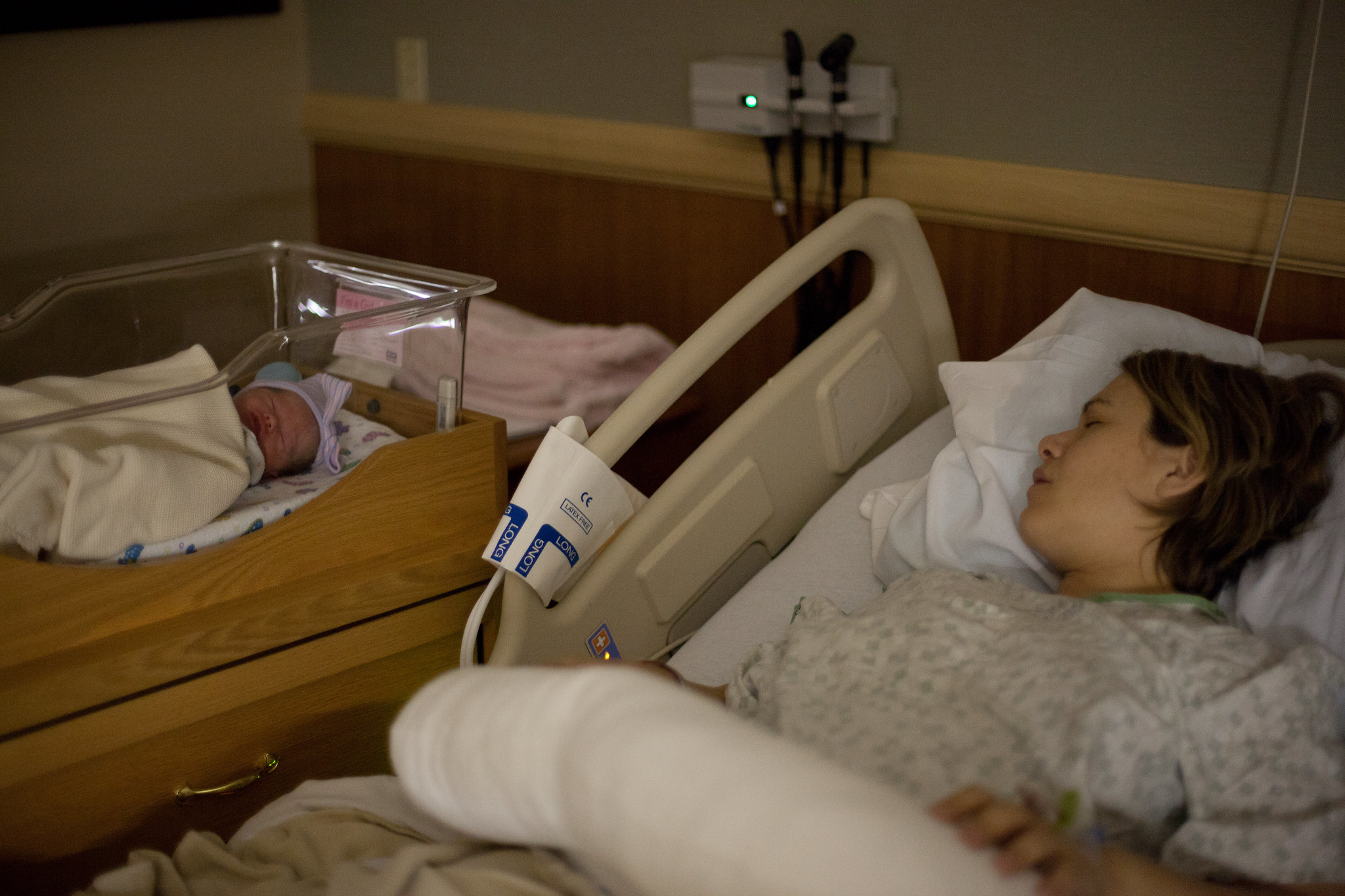Une femme dormant dans un lit d'hôpital avec son nouveau-né endormi à côté d'elle dans un berceau | Source : Flickr