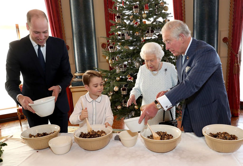 Le prince William, duc de Cambridge, le prince George, la reine Elizabeth II et le prince Charles, prince de Galles préparent des puddings de Noël spéciaux dans la salle de musique de Buckingham Palace, dans le cadre du lancement de l'initiative Ensemble à Noël de la Royal British Legion. | Photo: Getty Images