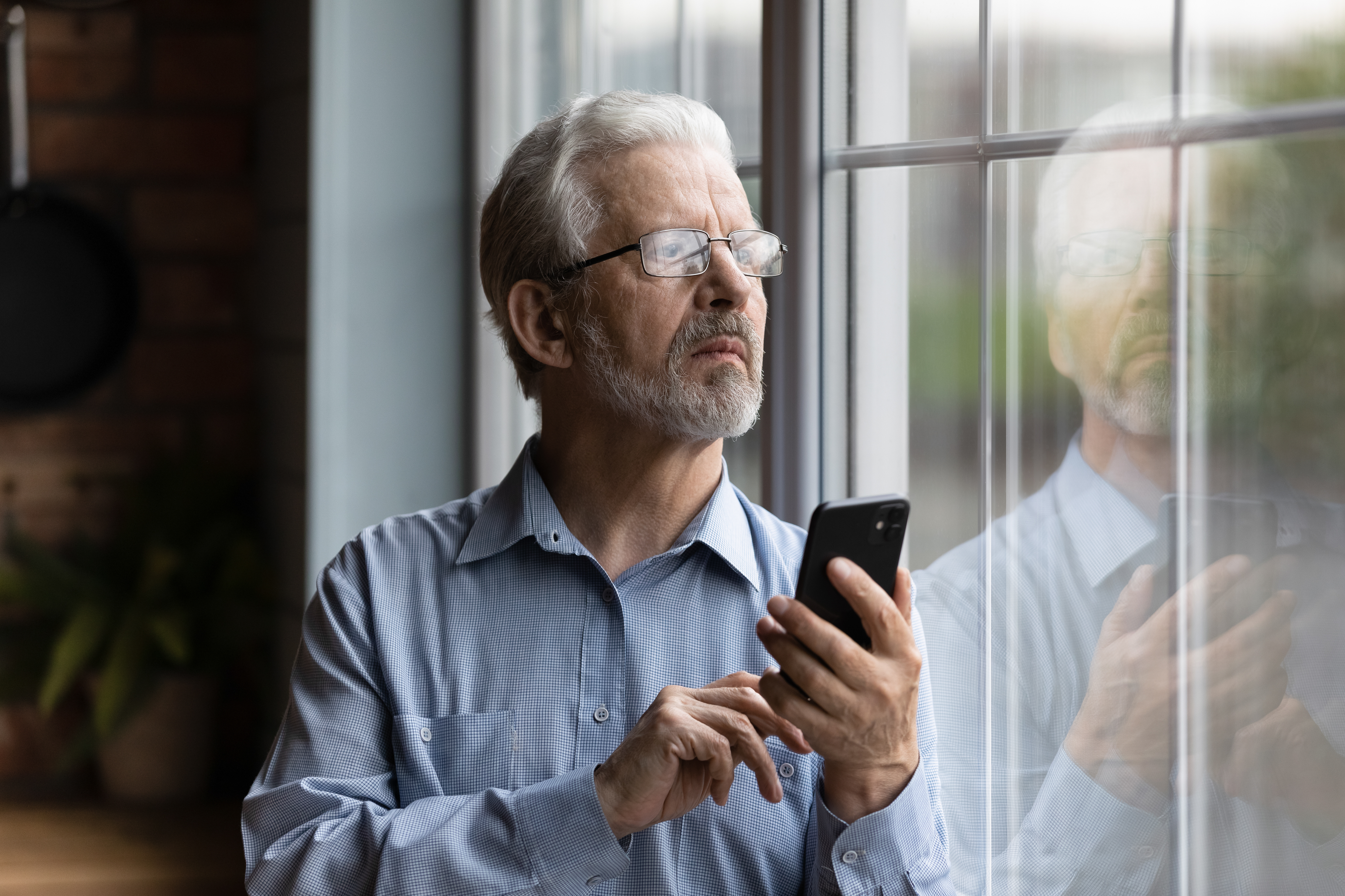 Un homme regardant par la fenêtre, un téléphone à la main | Source : Shutterstock