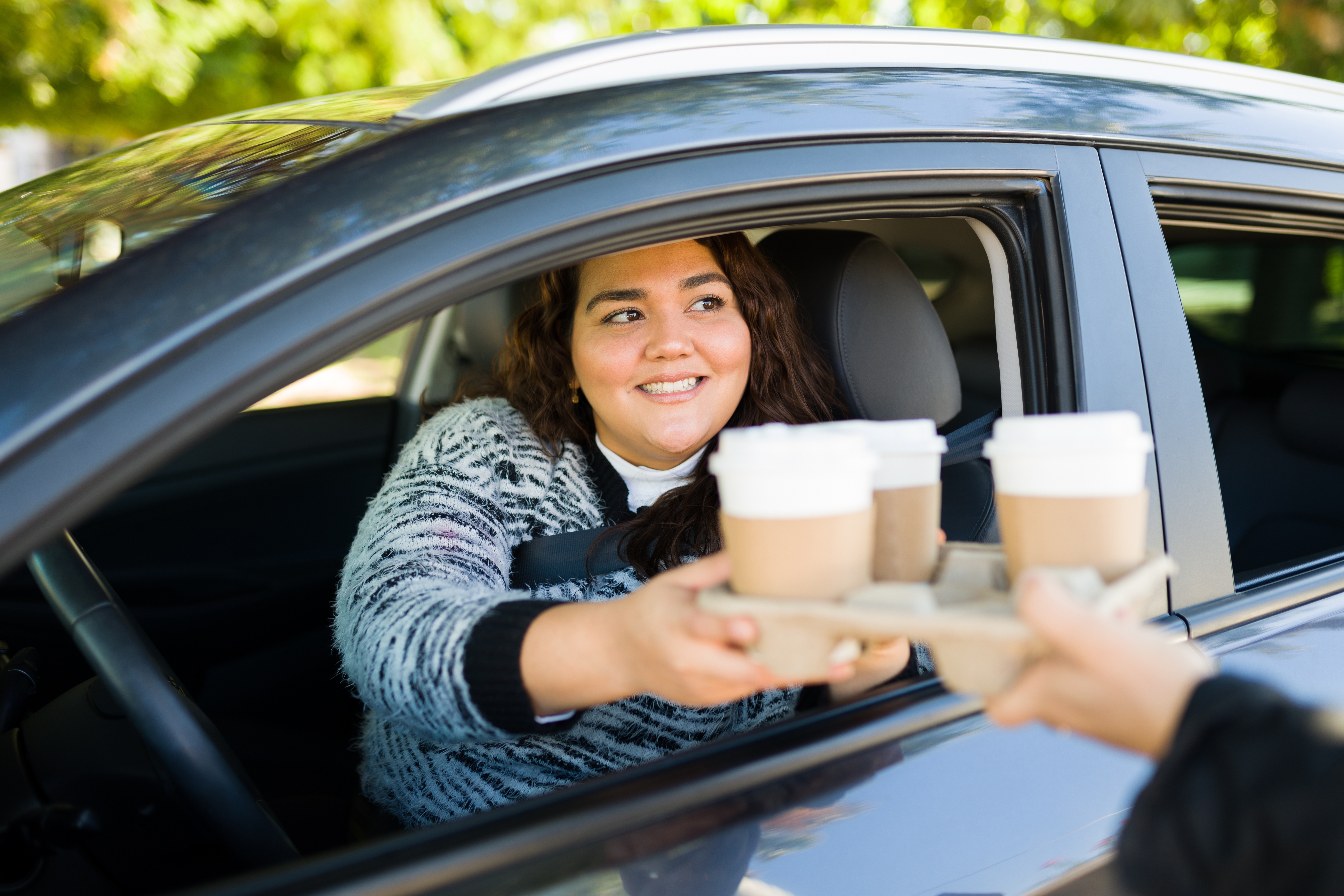 Femme conduisant sa voiture dans un drive thru pour acheter du café | Source : Shutterstock