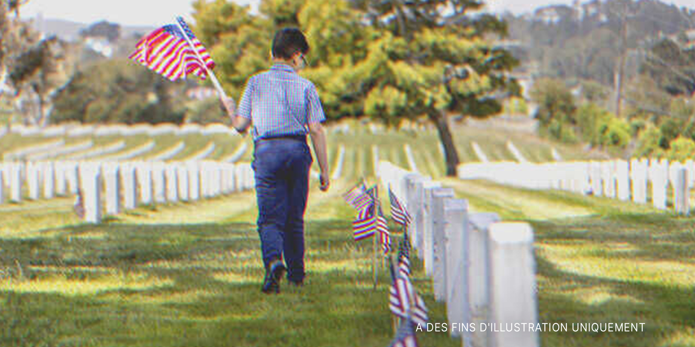 Garçon avec le drapeau national américain dans un cimetière | Source : Getty Images