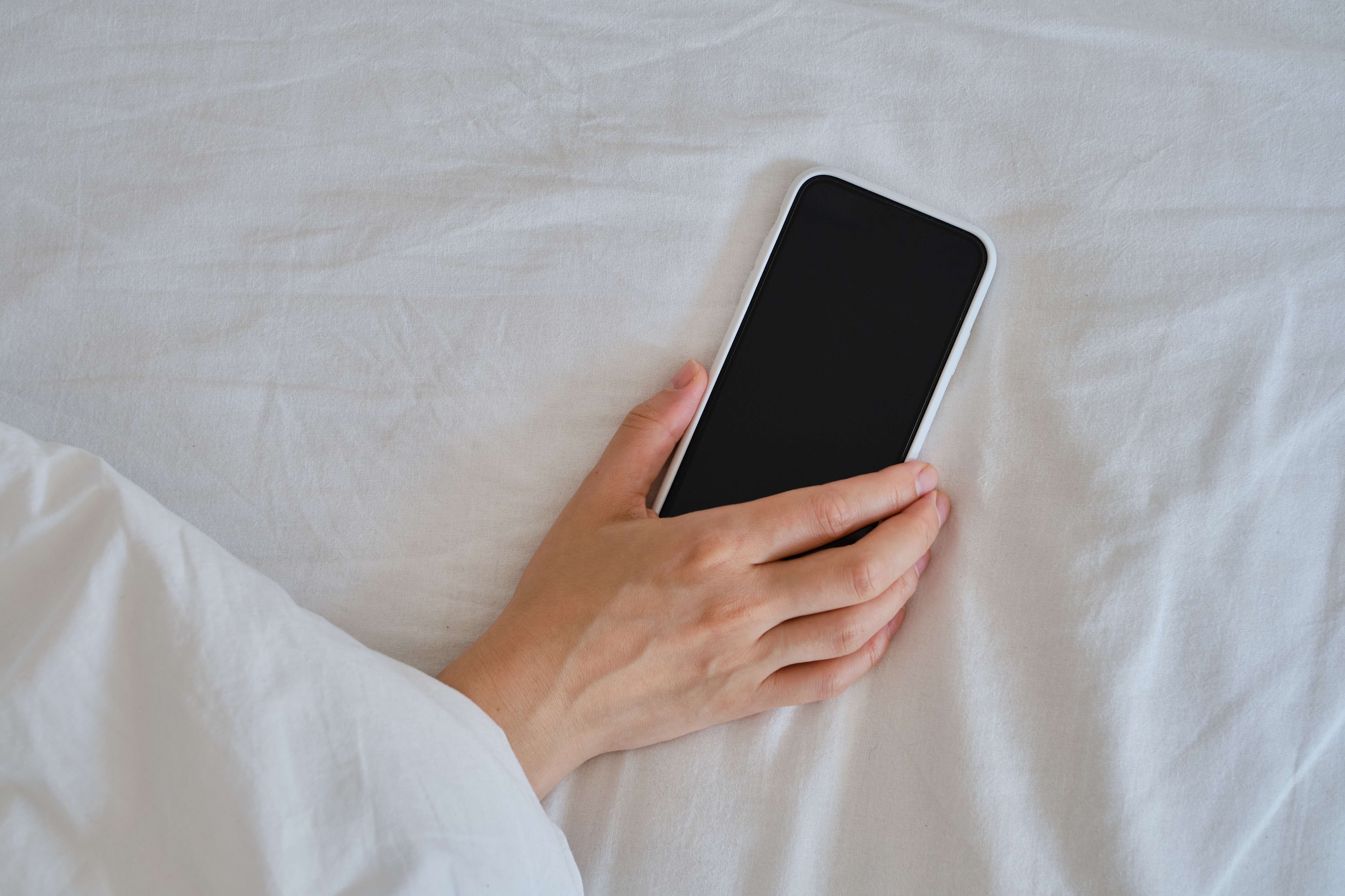 Gros plan d'une main tenant un smartphone au lit | Source : Shutterstock