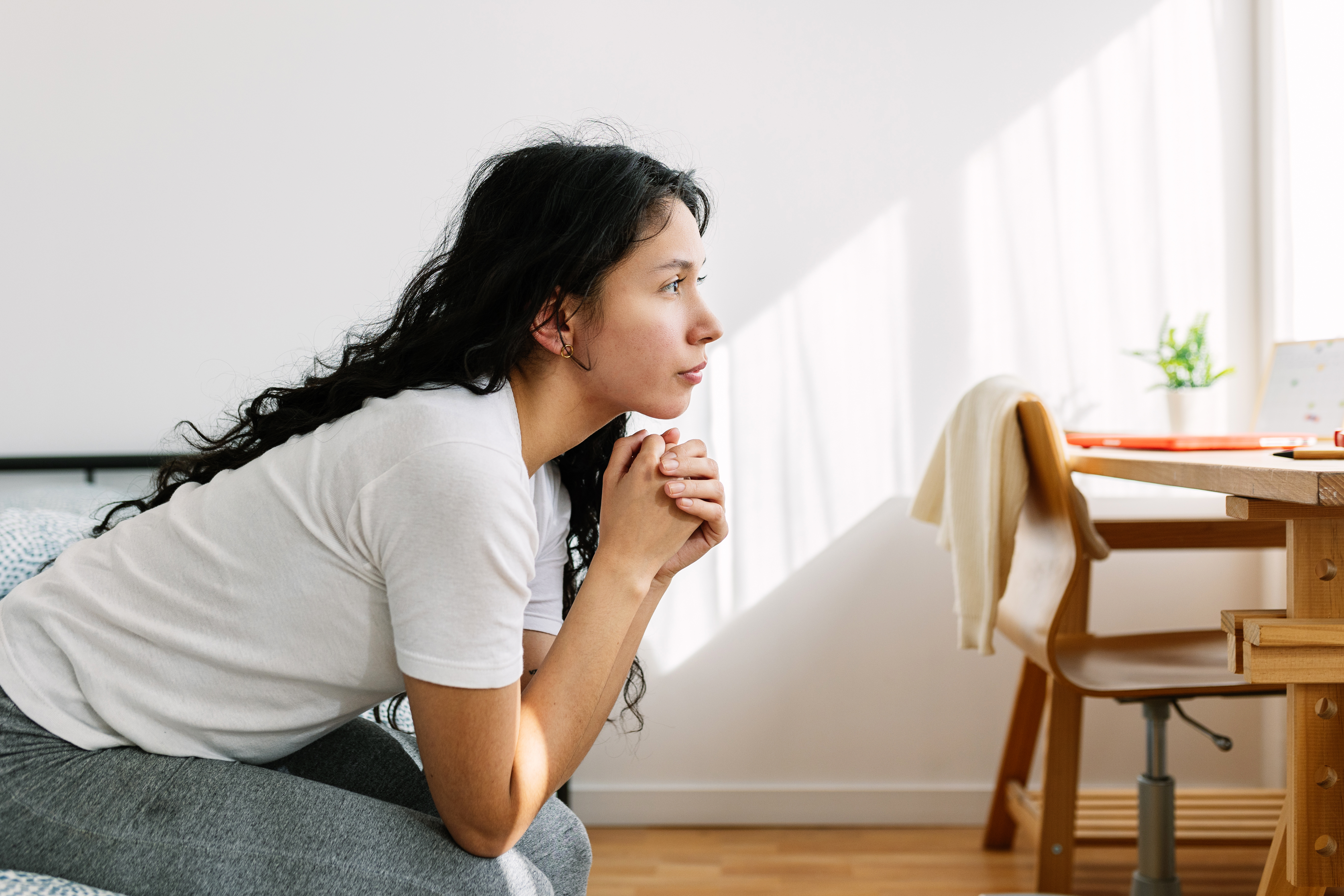 Triste et solitaire adolescente pensive regardant au loin assis sur le lit dans la chambre. Problème social et concept d'intimidation à l'adolescence | Source : Getty Images