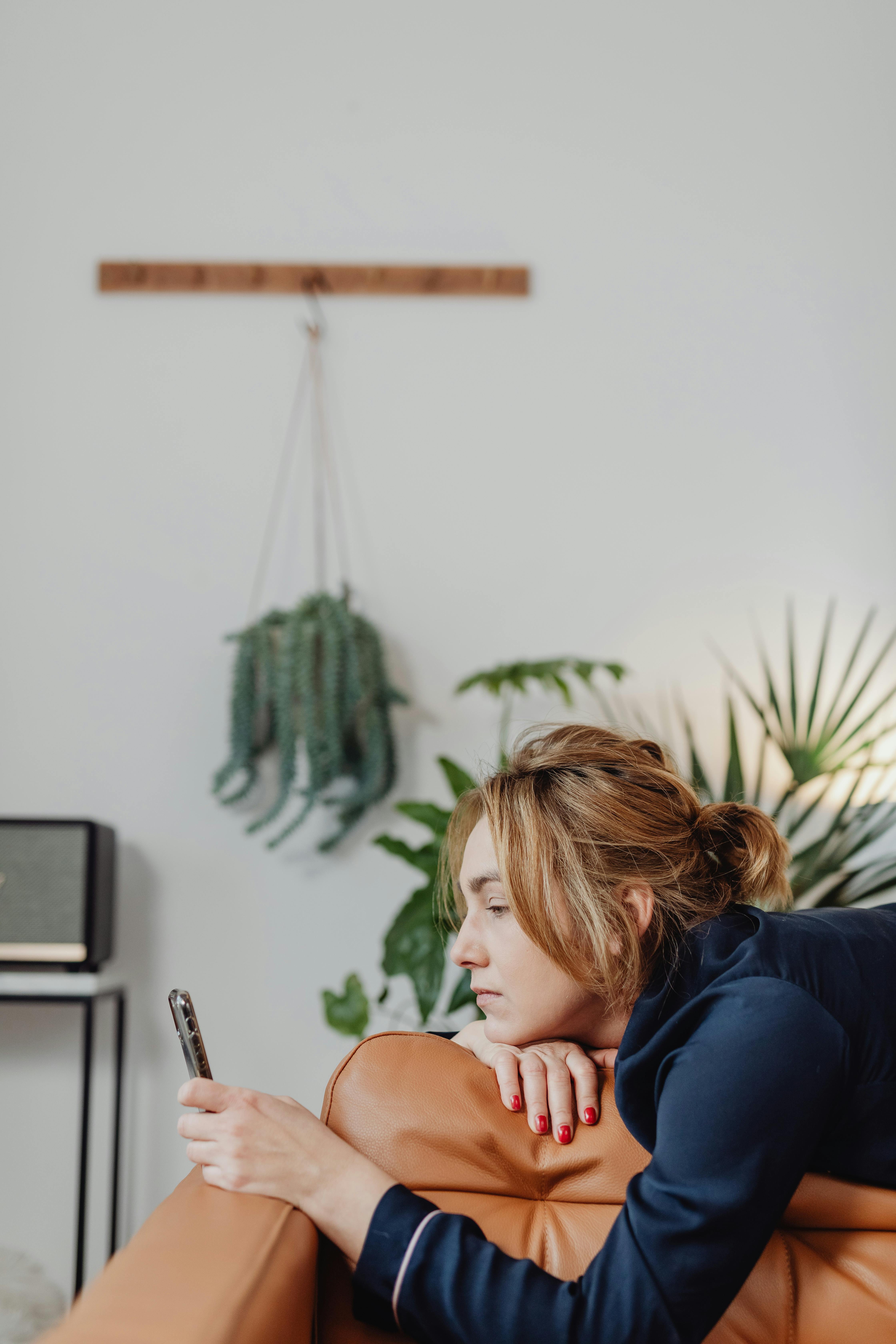 Femme allongée sur un canapé en cuir marron regardant son téléphone portable | Source : Pexels