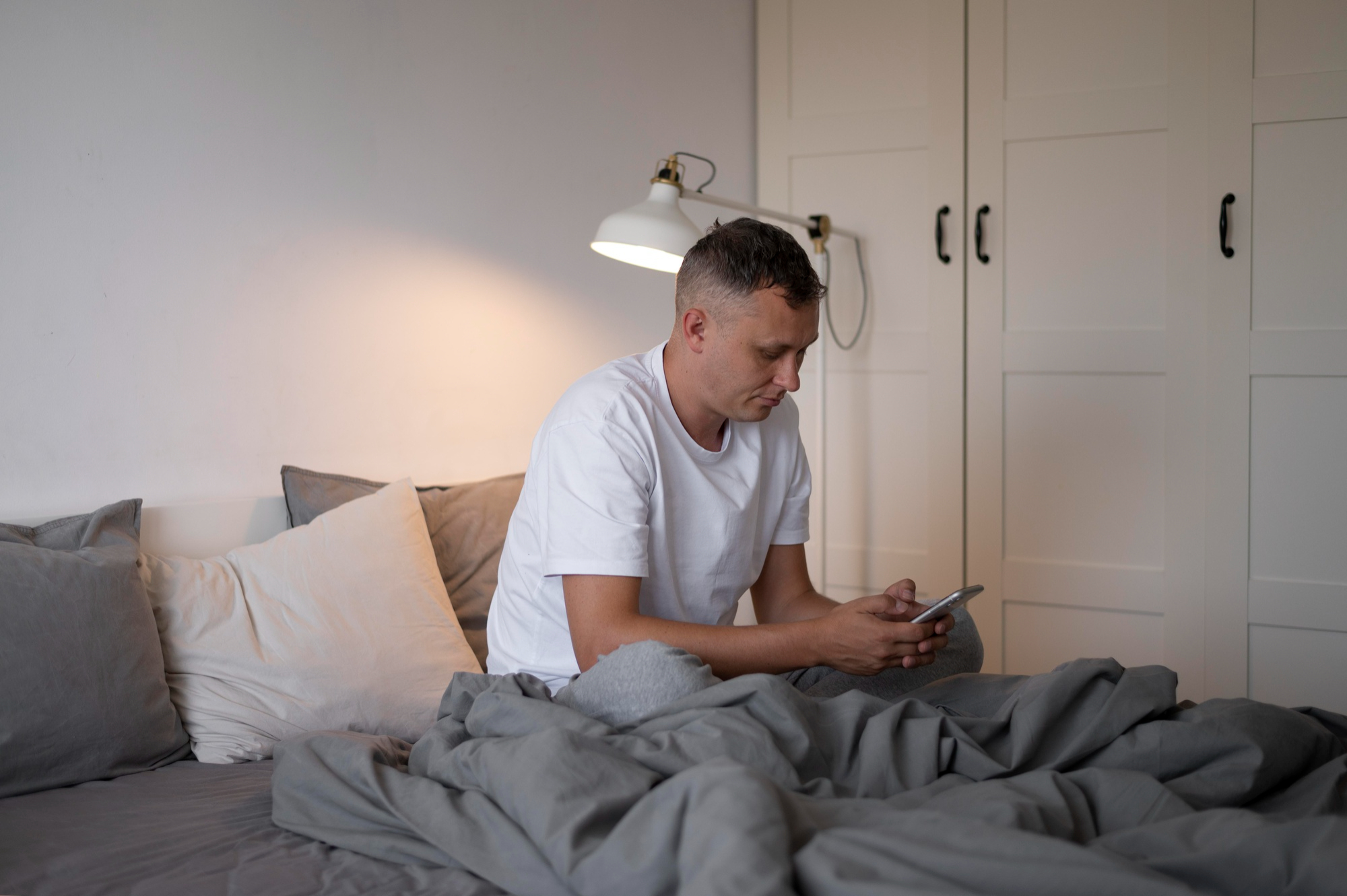 Un homme qui regarde un téléphone alors qu'il est recouvert d'un drap dans son lit | Source : Freepik