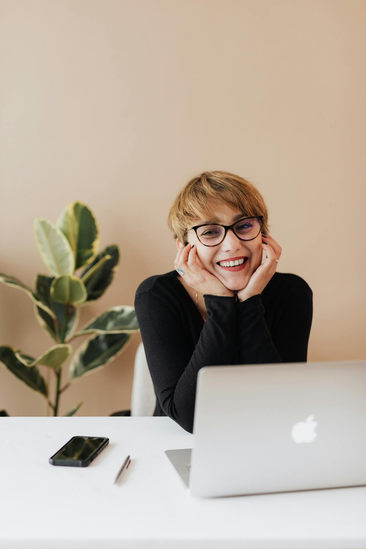 Une femme sourit alors qu'elle est assise à une table avec son ordinateur portable | Source : Pexels
