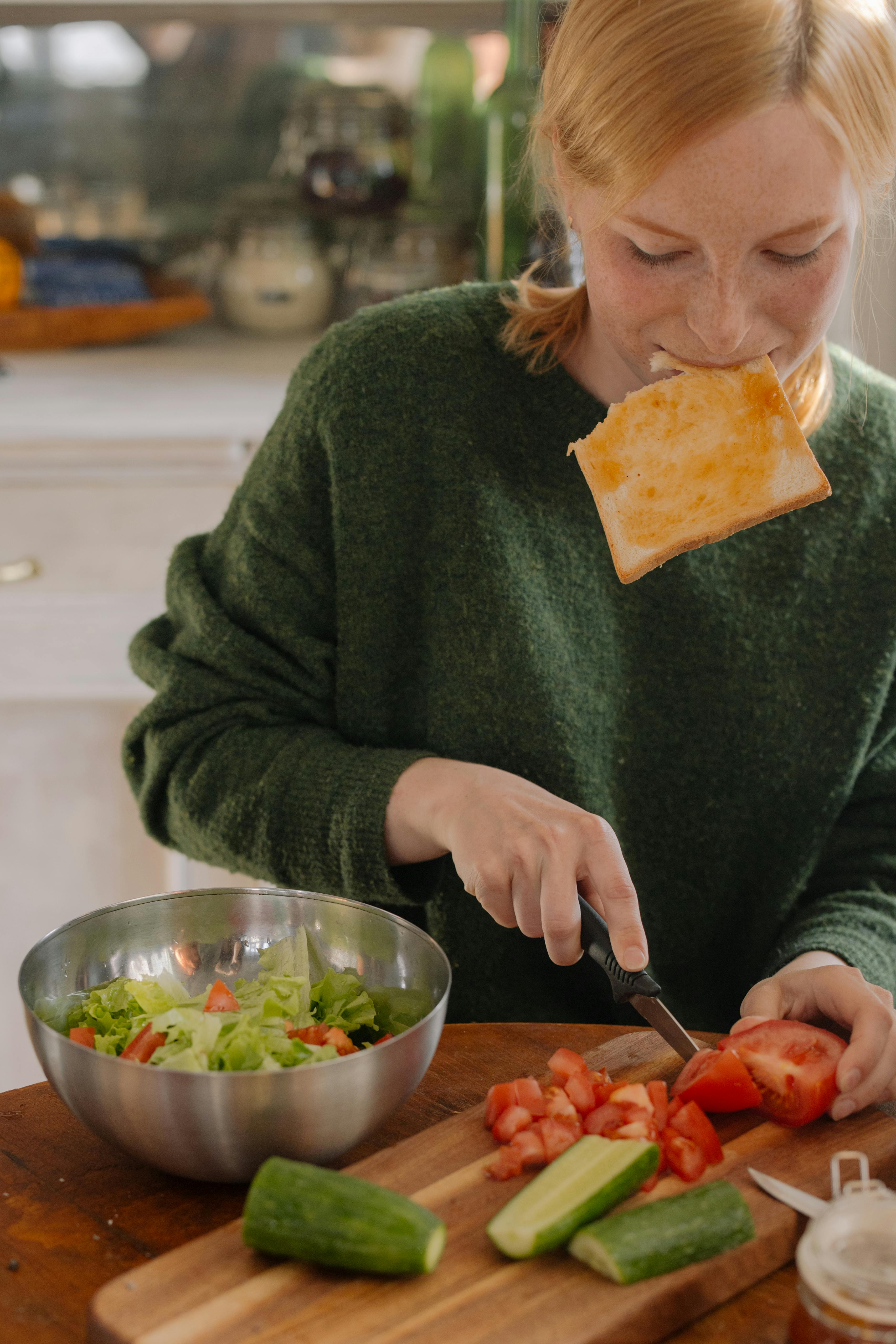 Une femme mangeant et coupant des légumes | Source : Pexels