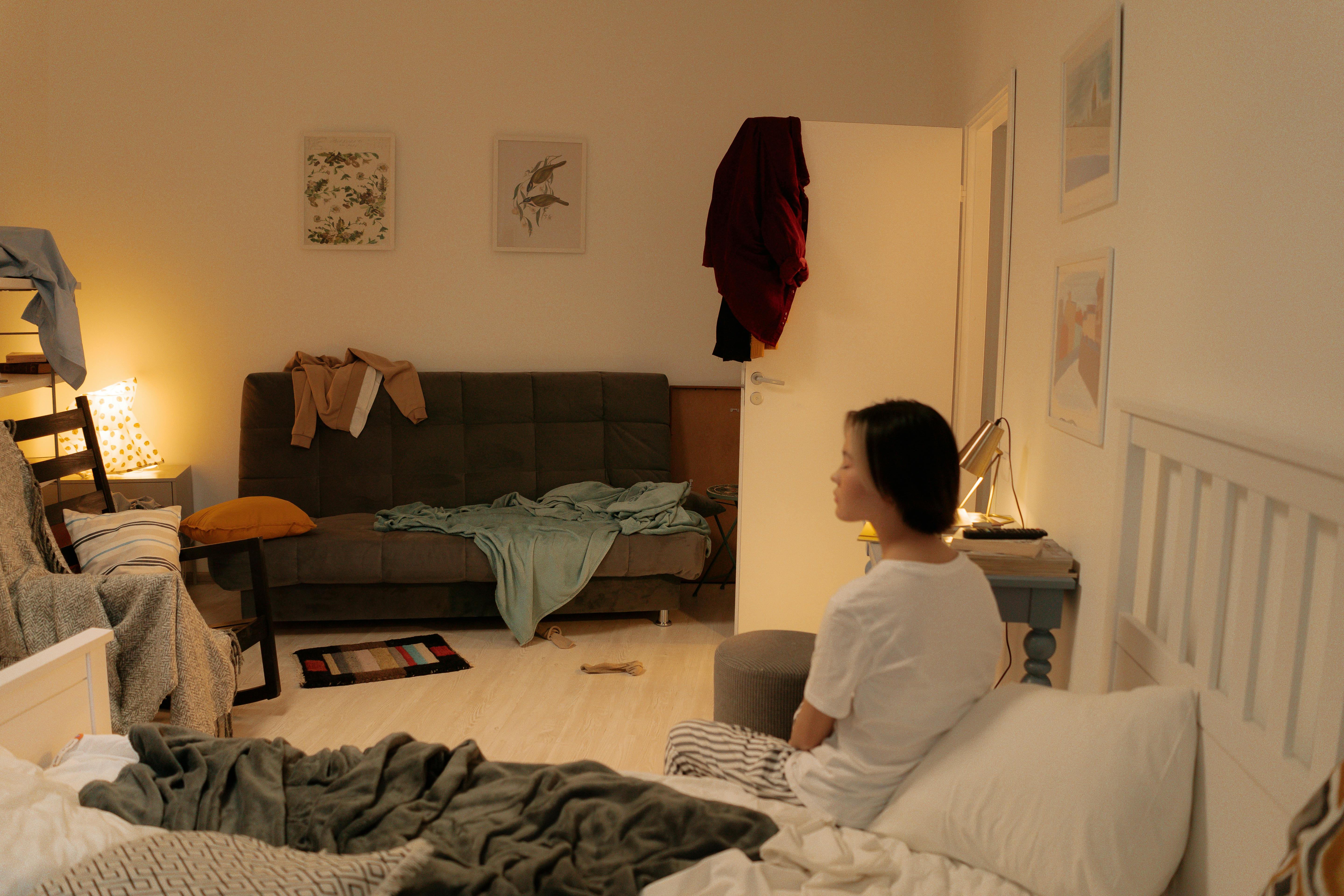 Une chambre à coucher en désordre avec une femme assise sur le lit | Source : Pexels