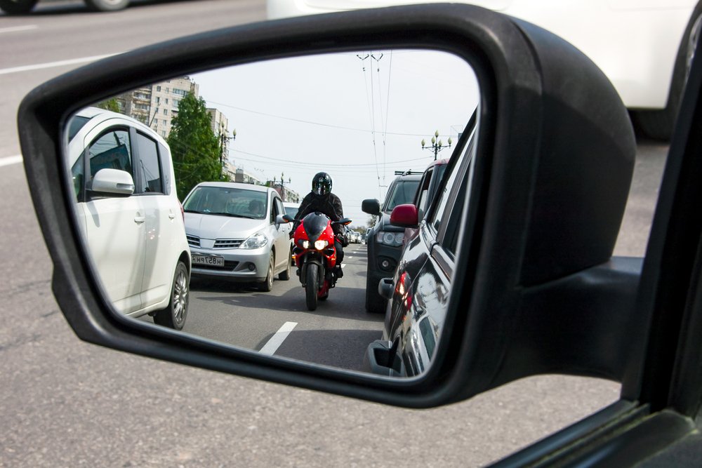 Une moto rouge, sportive, se déplace entre les voies, dangereusement près des voitures | Source : Shutterstock